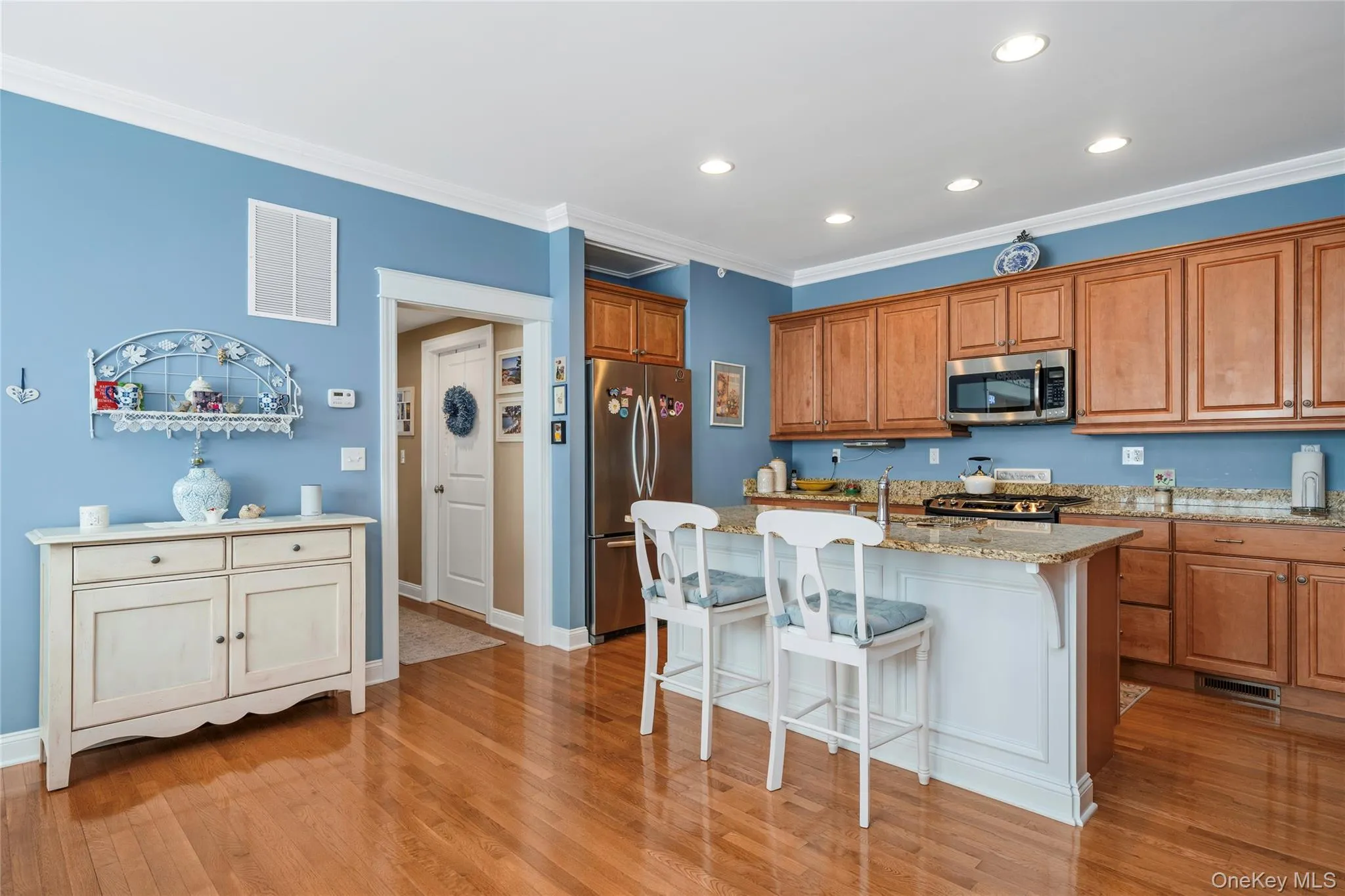 Kitchen featuring wood finish cabinetry, stainless steel appliances, a breakfast bar area, ornamental molding, and light stone countertops Kitchen featuring wood finish cabinetry, stainless steel appliances, a breakfast bar area, ornamental molding, and light stone countertops