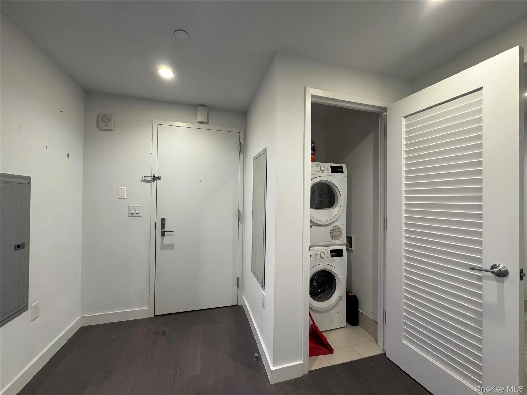 Laundry area with dark wood-style floors, stacked washer / dryer, and electric panel Laundry area with dark wood-style floors, stacked washer / dryer, and electric panel