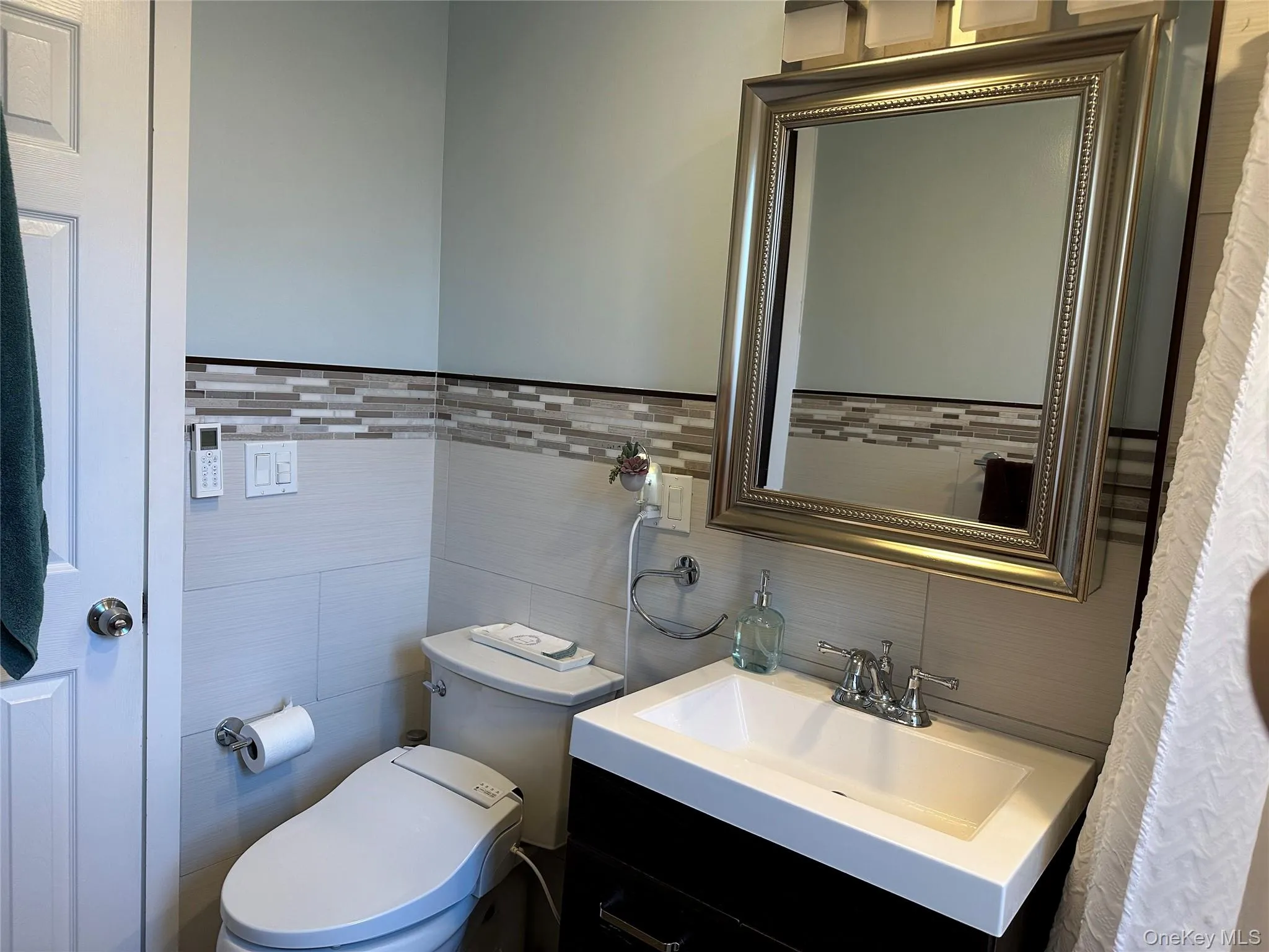 Bathroom featuring vanity, toilet, tile walls, and tasteful backsplash Bathroom featuring vanity, toilet, tile walls, and tasteful backsplash
