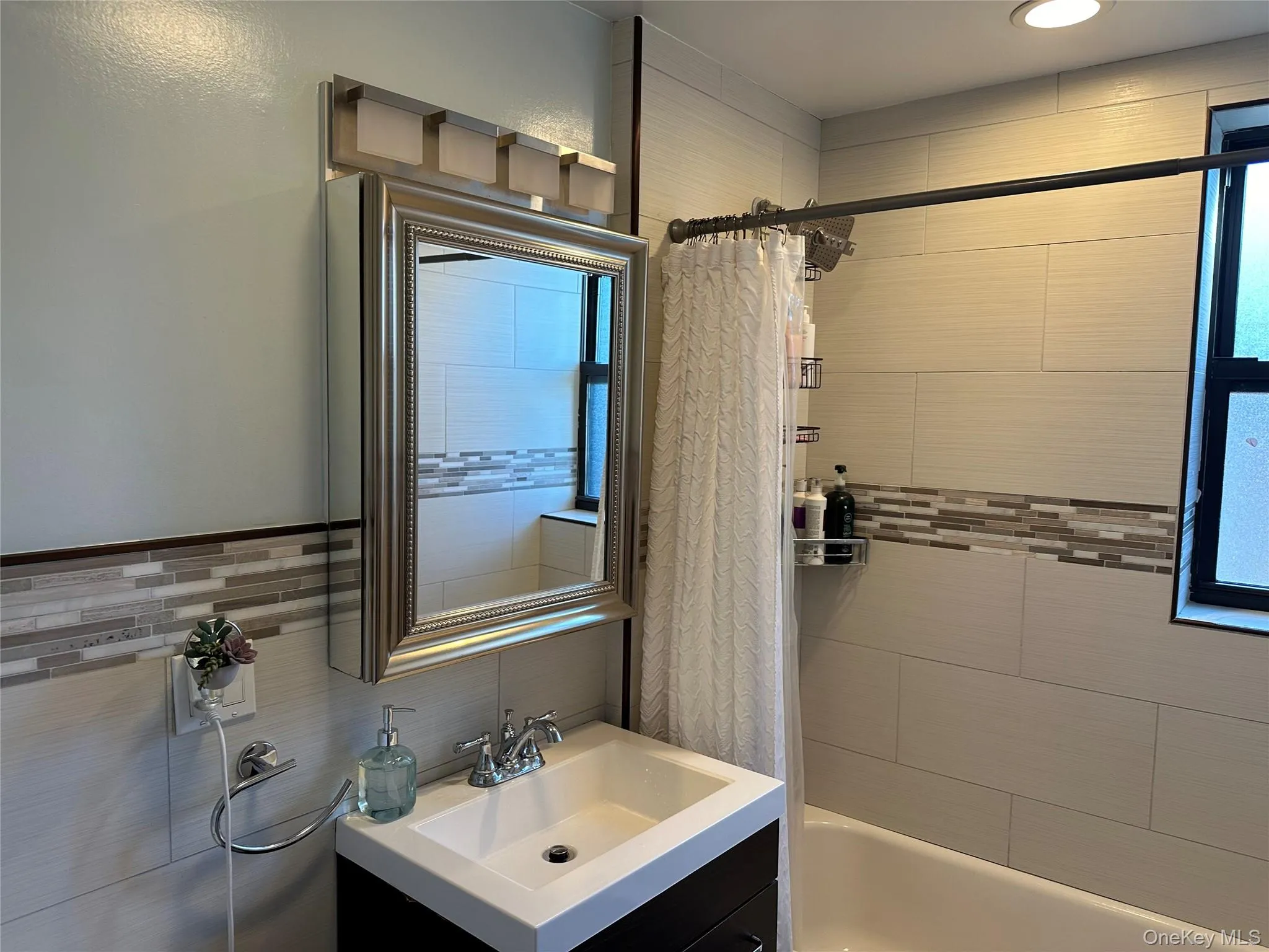 Bathroom with tasteful backsplash, vanity, and shower / bath combination with curtain Bathroom with tasteful backsplash, vanity, and shower / bath combination with curtain