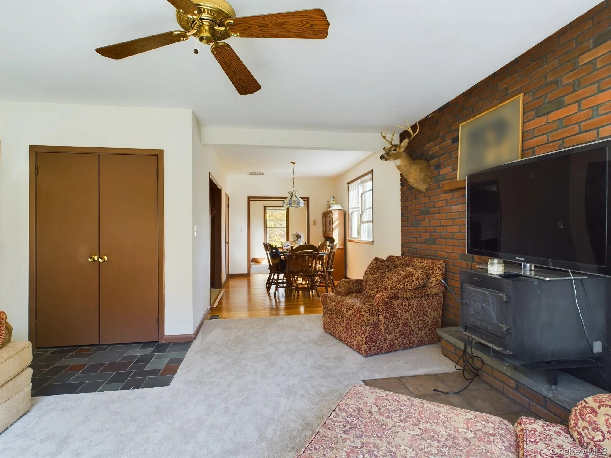 Carpeted living area featuring a wood stove, a ceiling fan, and brick wall Carpeted living area featuring a wood stove, a ceiling fan, and brick wall
