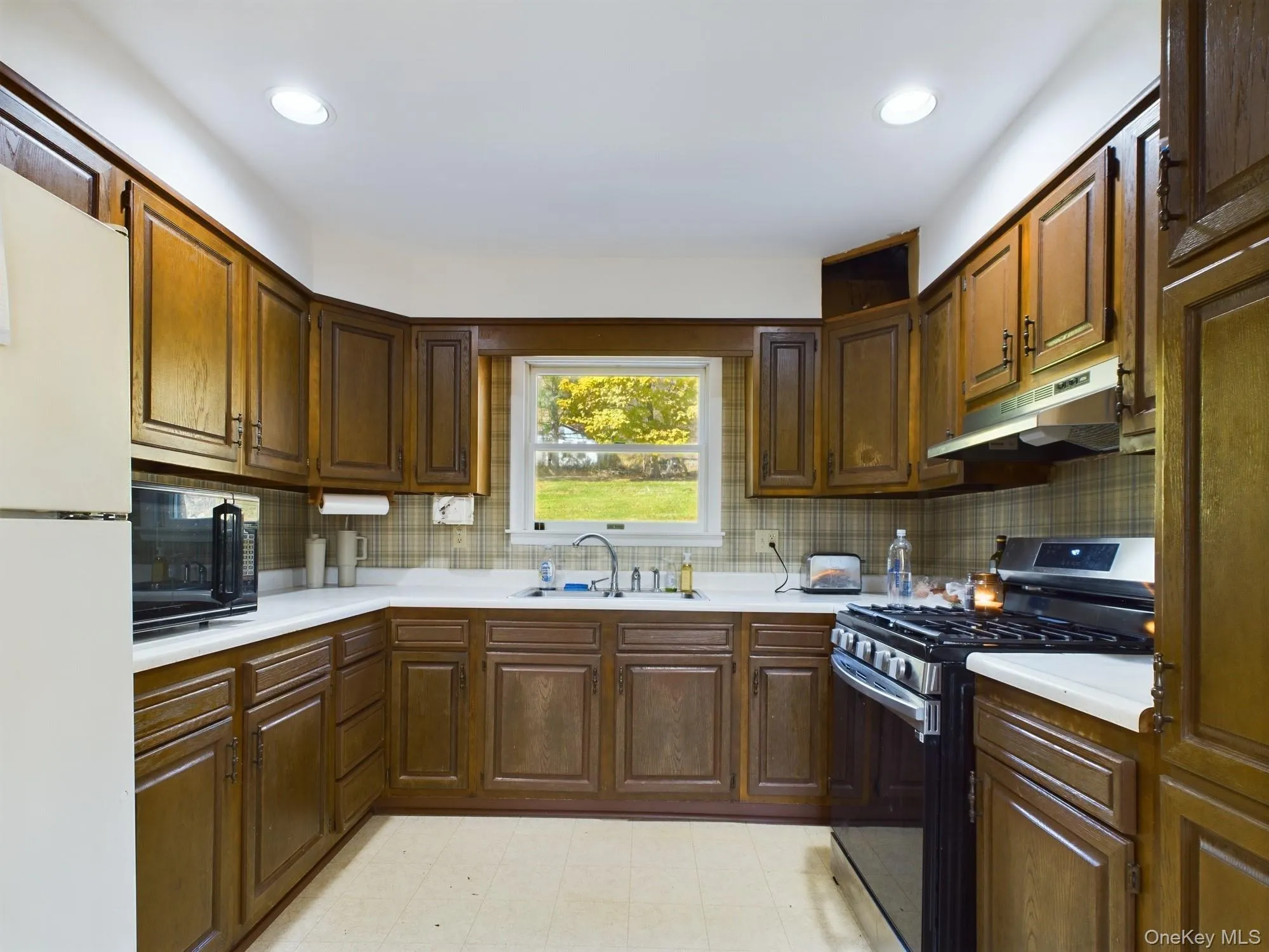 Kitchen with gas range, freestanding refrigerator, light countertops, under cabinet range hood, and black microwave Kitchen with gas range, freestanding refrigerator, light countertops, under cabinet range hood, and black microwave