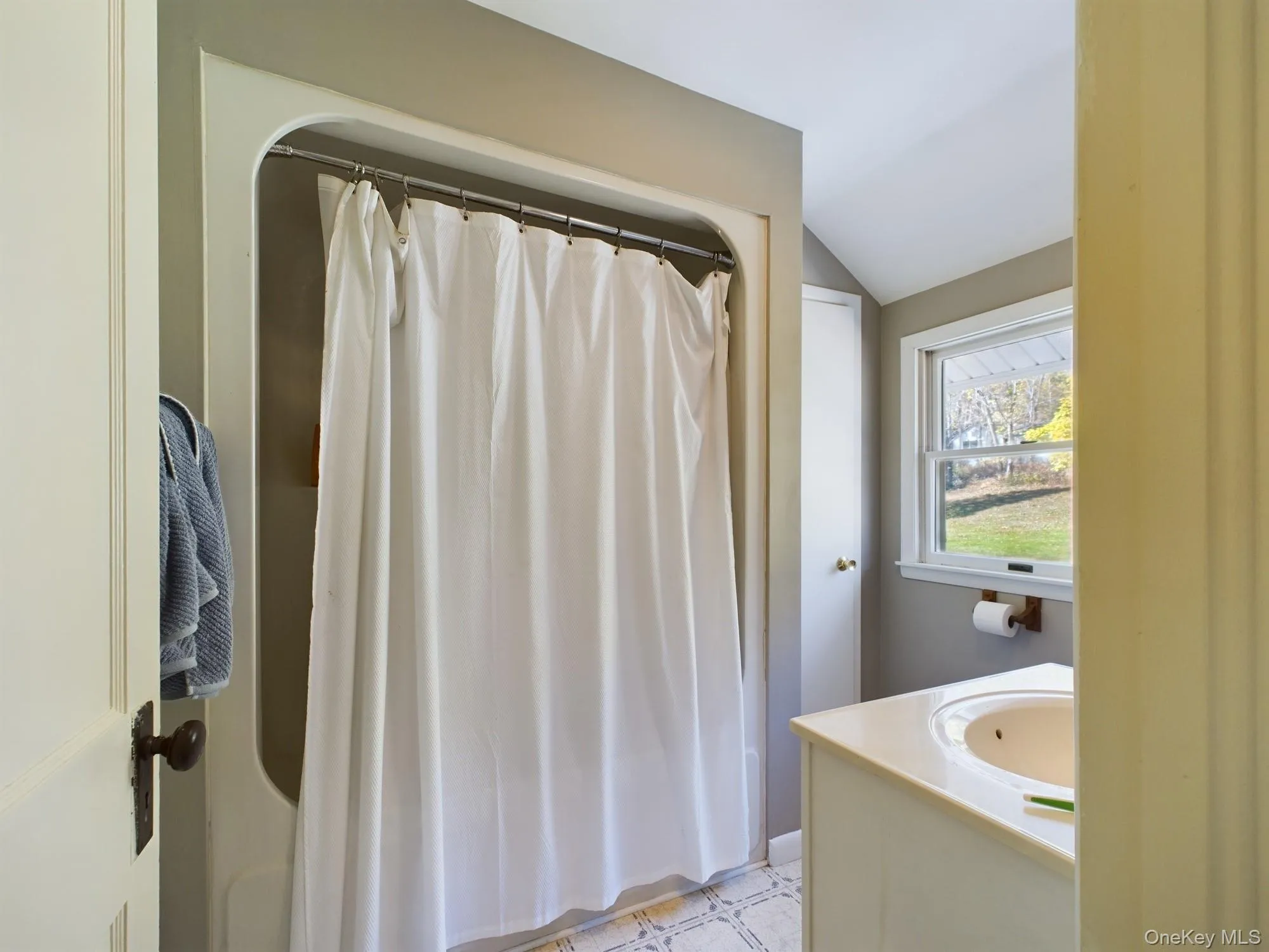 Bathroom with lofted ceiling, a shower with shower curtain, vanity, and tile patterned floors Bathroom with lofted ceiling, a shower with shower curtain, vanity, and tile patterned floors