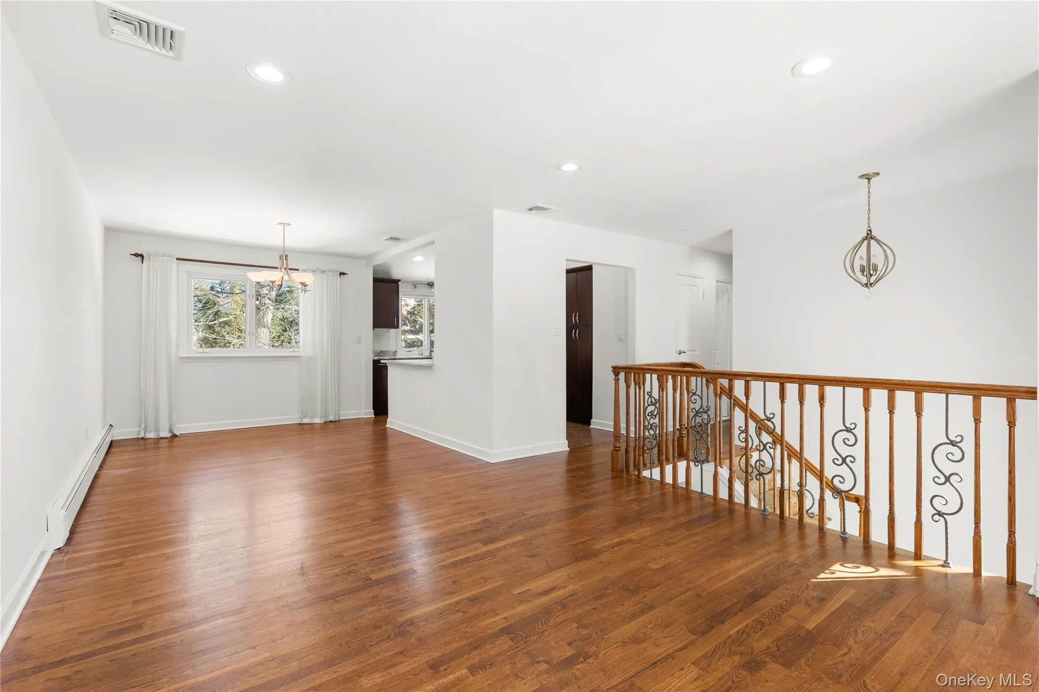 Living room and dining room featuring a chandelier, baseboard heating, and wood finished floors Living room and dining room featuring a chandelier, baseboard heating, and wood finished floors