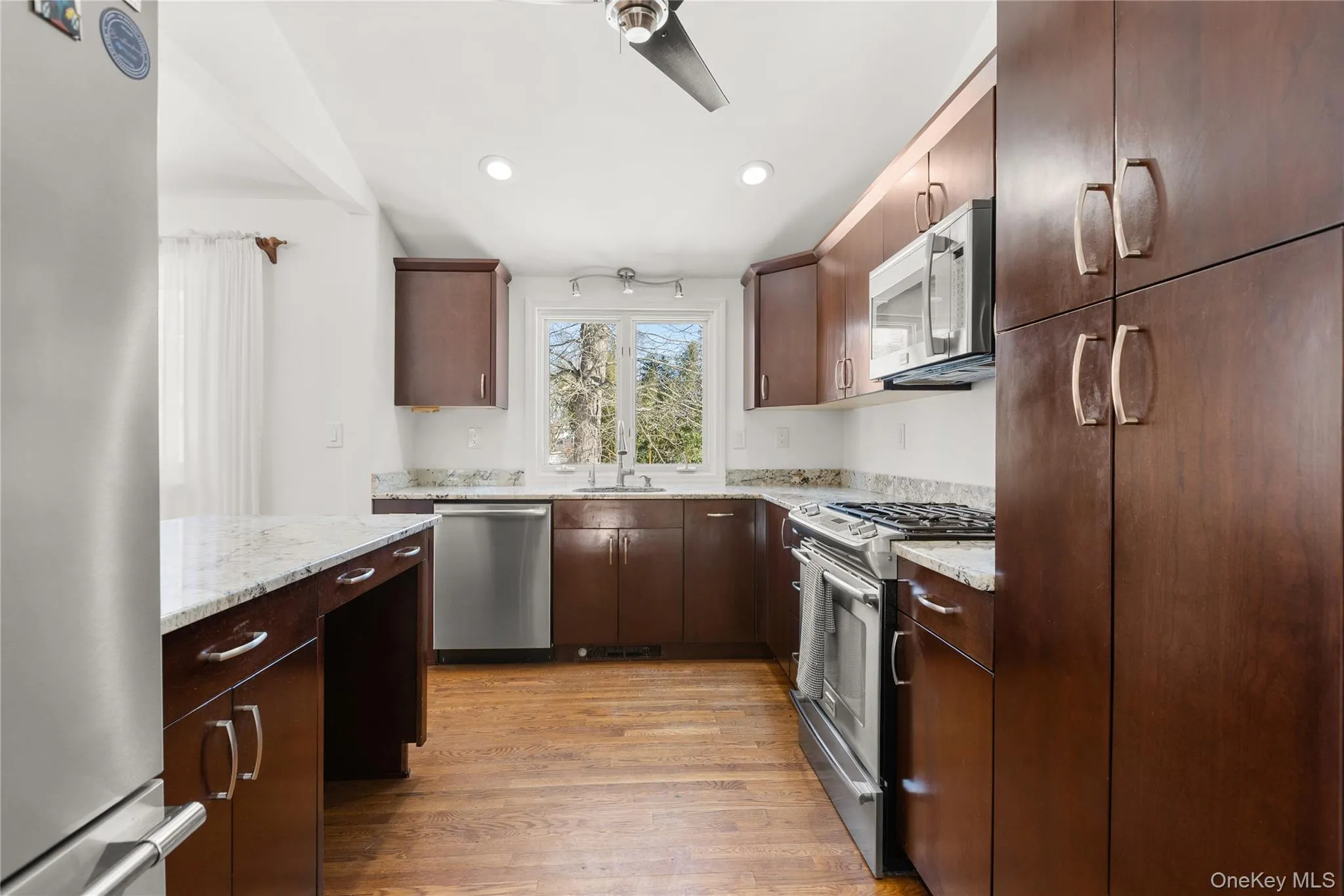 Kitchen featuring stainless steel appliances, dark wood finish cabinetry, light granite countertops, wood floors, and recessed lighting Kitchen featuring stainless steel appliances, dark wood finish cabinetry, light granite countertops, wood floors, and recessed lighting