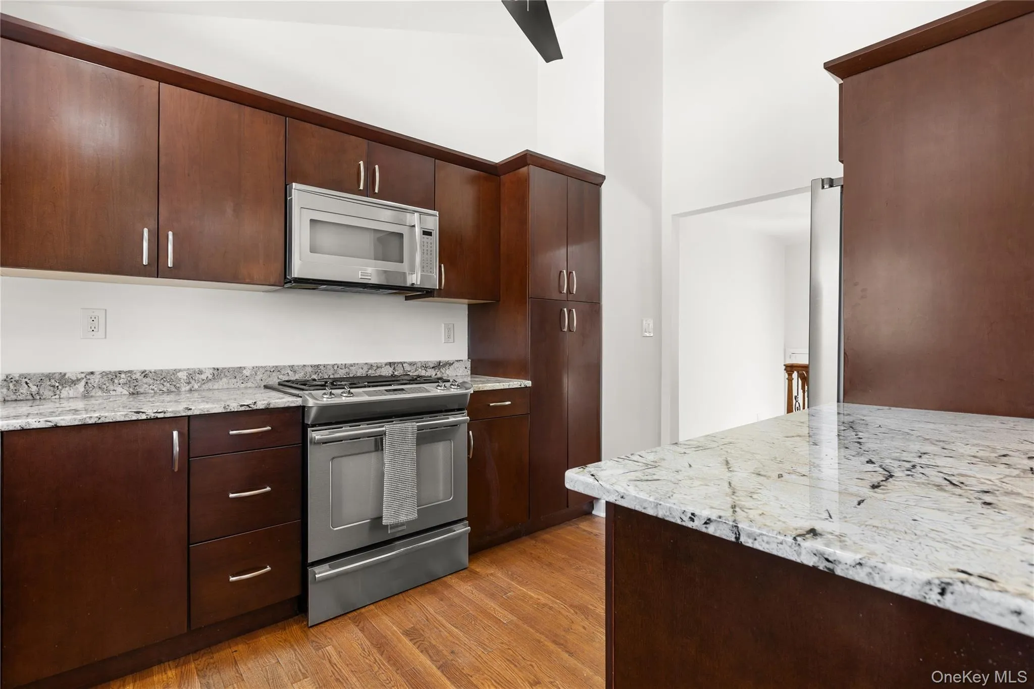 Kitchen with stainless steel gas range, dark wood finish cabinets, white microwave, granite counters, and lofted ceiling Kitchen with stainless steel gas range, dark wood finish cabinets, white microwave, granite counters, and lofted ceiling