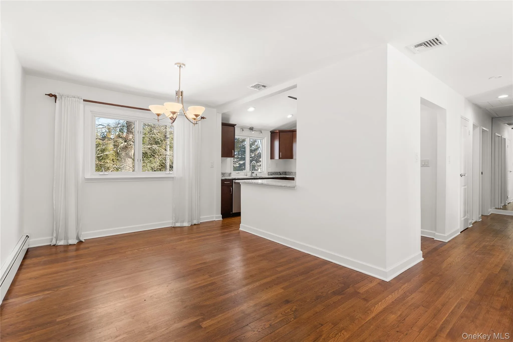Dining area open to kitchen with wood flooring and light fixture Dining area open to kitchen with wood flooring and light fixture