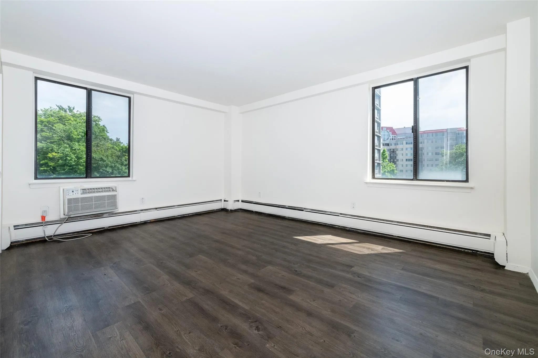 Unfurnished room featuring plenty of natural light, dark wood-type flooring, a baseboard heating unit, and baseboard heating Unfurnished room featuring plenty of natural light, dark wood-type flooring, a baseboard heating unit, and baseboard heating