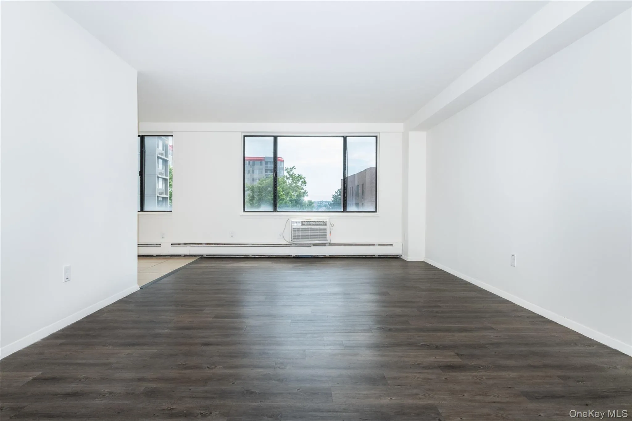 Spare room with dark wood finished floors, an AC wall unit, and a baseboard heating unit Spare room with dark wood finished floors, an AC wall unit, and a baseboard heating unit