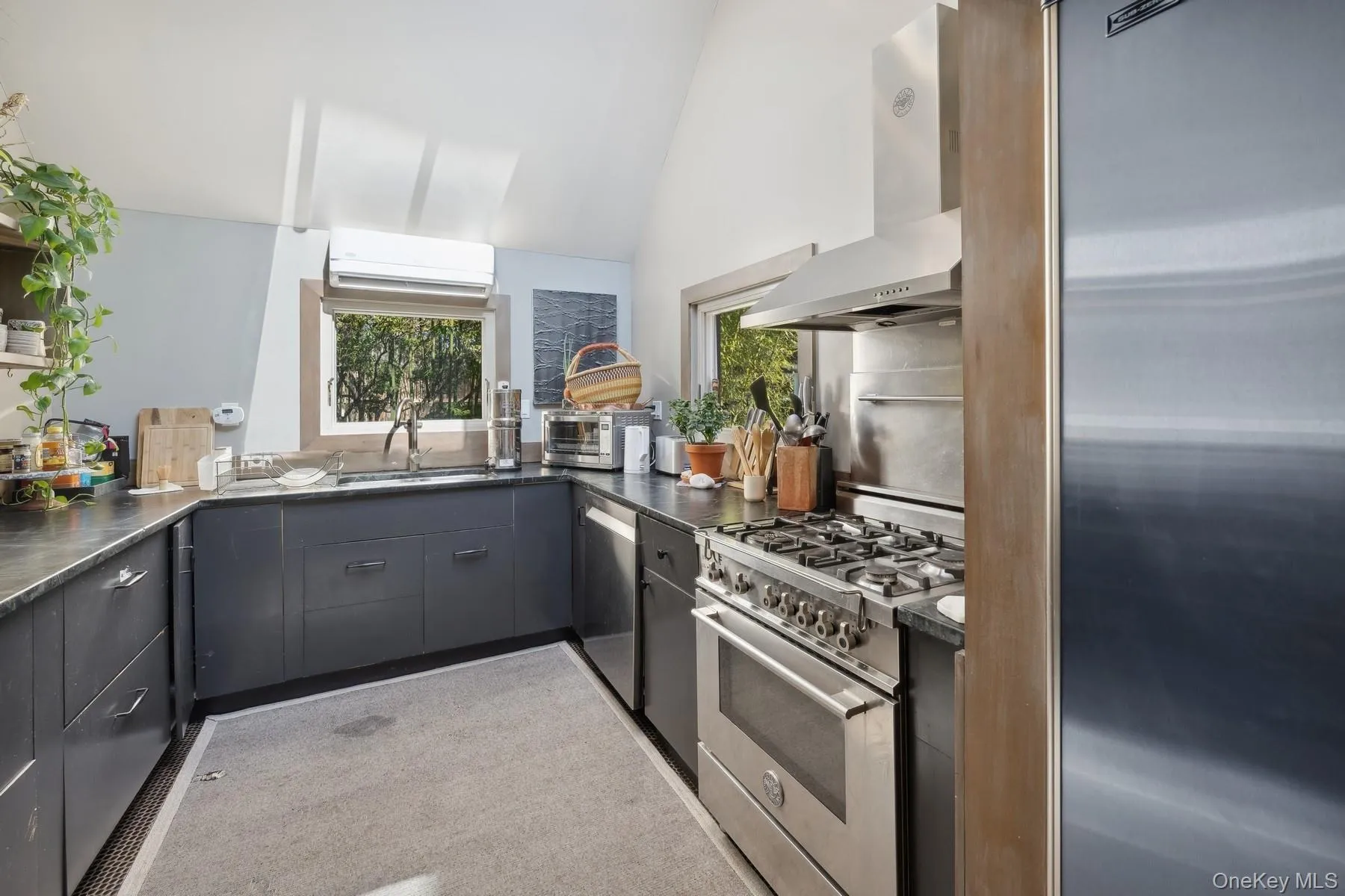 Kitchen with sink, wall chimney exhaust hood, gray cabinets, a wall mounted AC, and appliances with stainless steel finishes Kitchen with sink, wall chimney exhaust hood, gray cabinets, a wall mounted AC, and appliances with stainless steel finishes