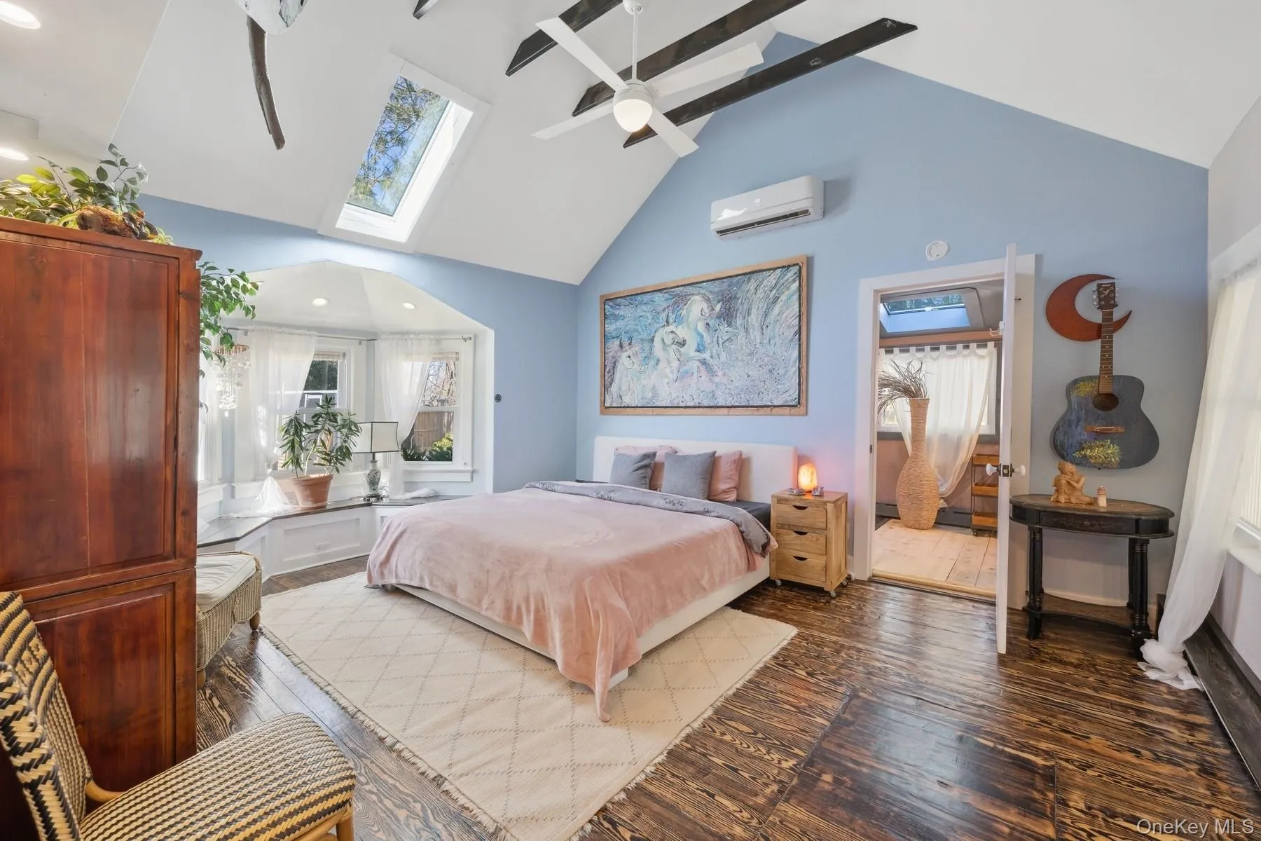 Bedroom featuring hardwood / wood-style flooring, ceiling fan, vaulted ceiling with skylight, and a wall mounted air conditioner Bedroom featuring hardwood / wood-style flooring, ceiling fan, vaulted ceiling with skylight, and a wall mounted air conditioner