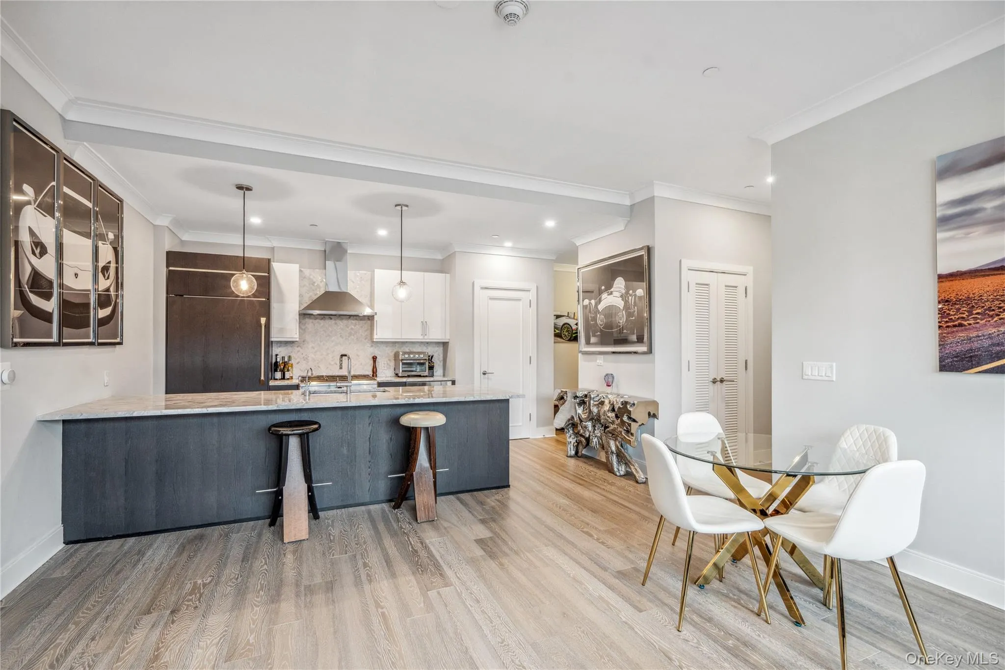 Kitchen with white cabinetry, wall chimney exhaust hood, built in fridge, kitchen peninsula, and decorative light fixtures Kitchen with white cabinetry, wall chimney exhaust hood, built in fridge, kitchen peninsula, and decorative light fixtures