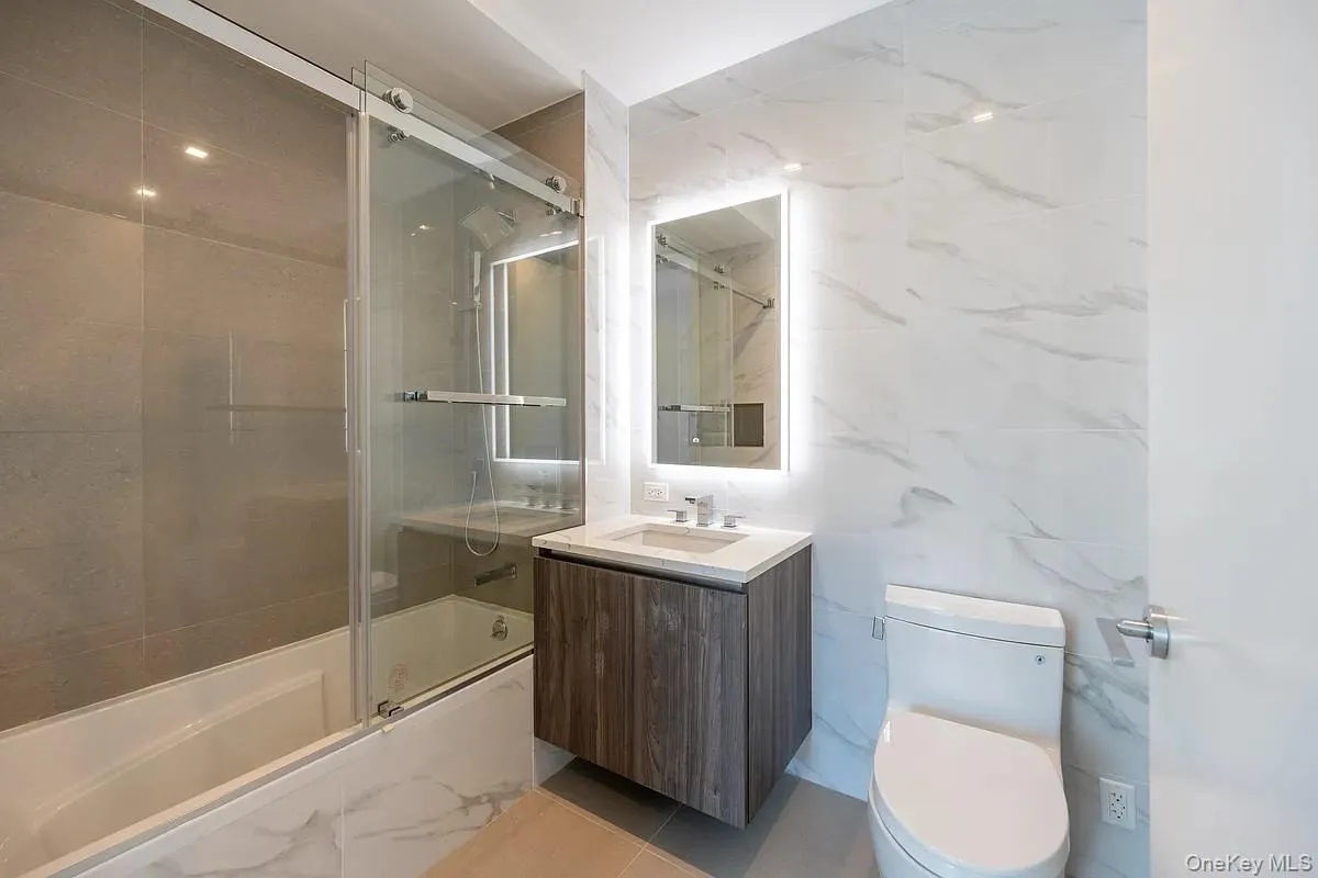 Full bath with vanity, tile walls, toilet, and shower / bath combination with glass door Full bath with vanity, tile walls, toilet, and shower / bath combination with glass door