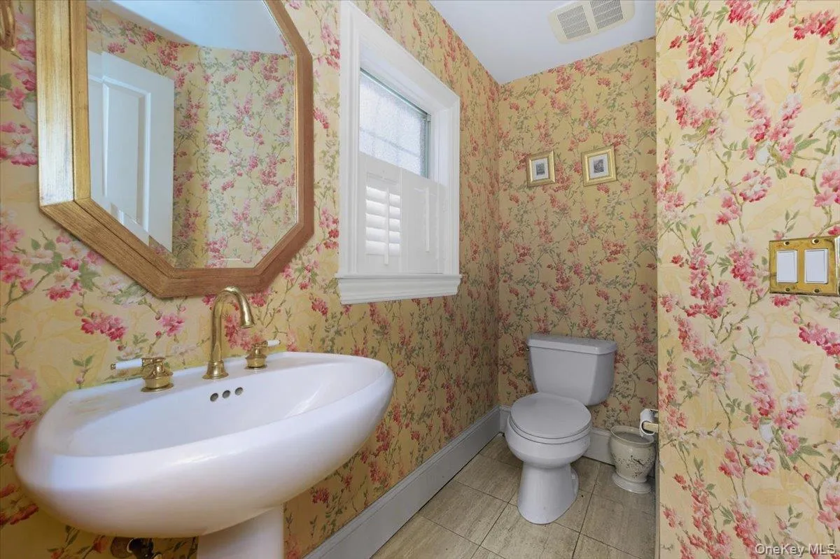 Main entry half bathroom featuring light tile patterned floors and wallpapered walls Main entry half bathroom featuring light tile patterned floors and wallpapered walls