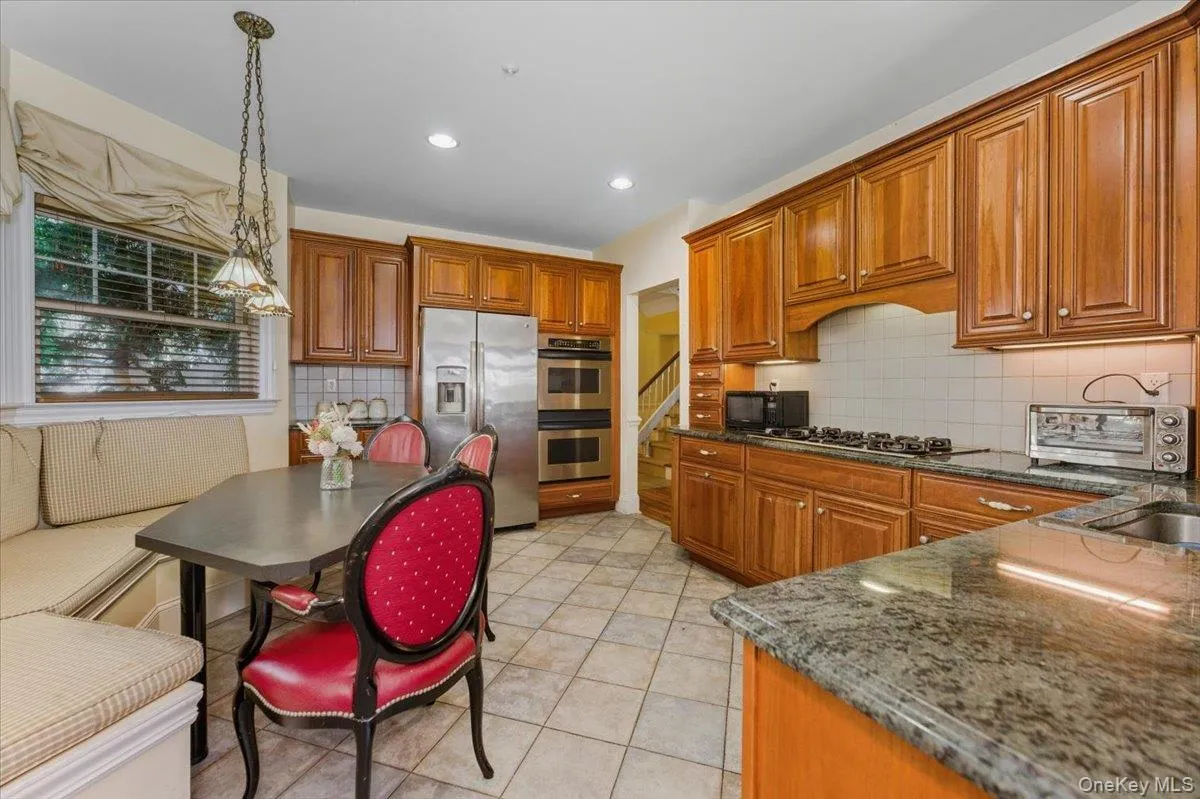 Kitchen with wood finish cabinets, stainless steel appliances, decorative light fixtures, dark stone counters, and light tile patterned flooring Kitchen with wood finish cabinets, stainless steel appliances, decorative light fixtures, dark stone counters, and light tile patterned flooring