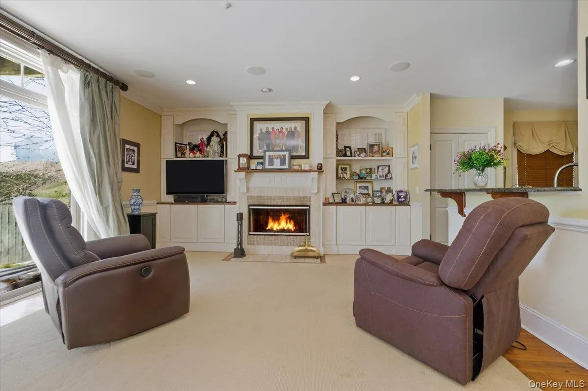 Living room featuring a fireplace with flush hearth, built in features, crown molding, and recessed lighting Living room featuring a fireplace with flush hearth, built in features, crown molding, and recessed lighting