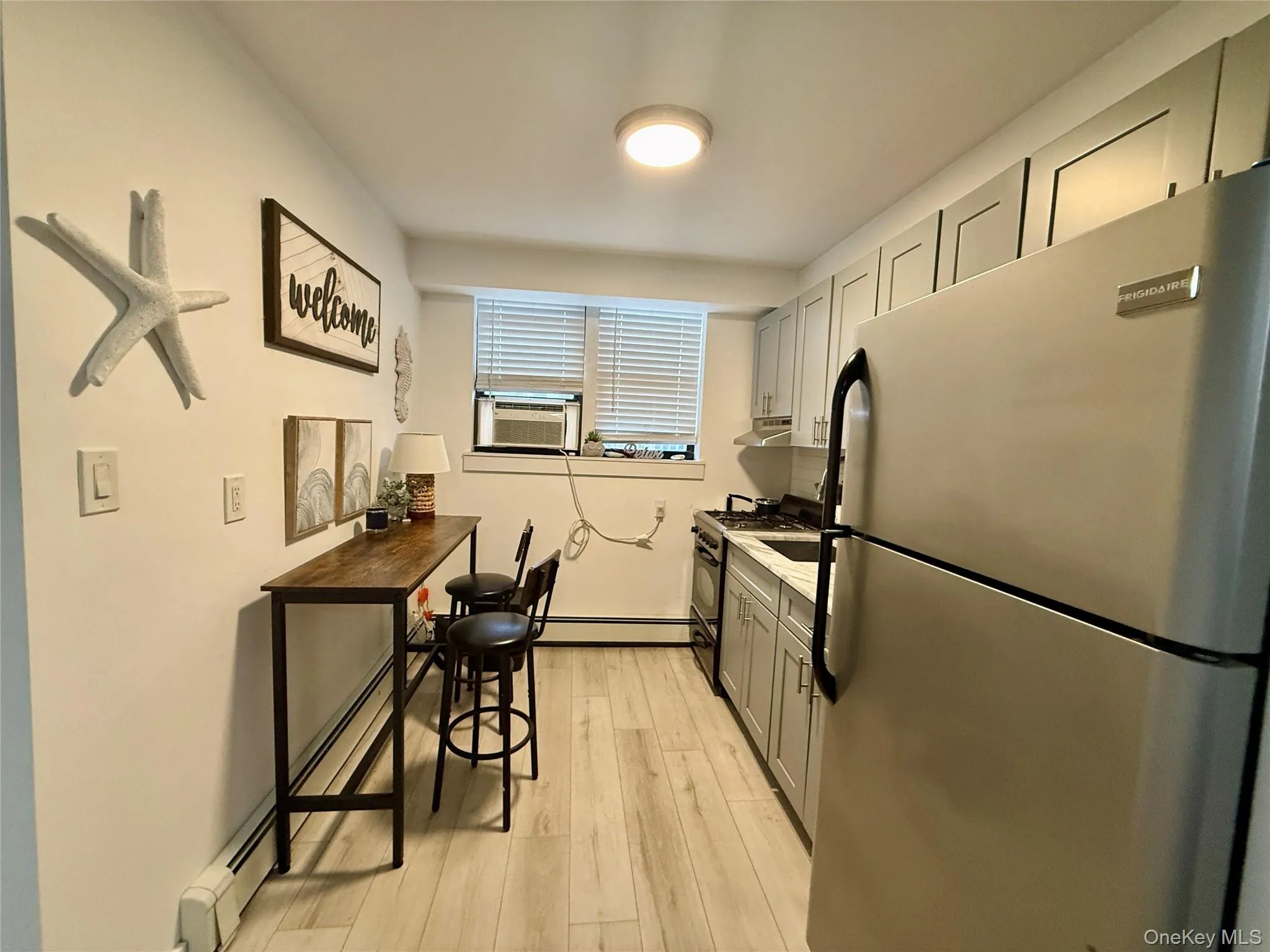Kitchen featuring freestanding refrigerator, light wood-type flooring, black gas range, a baseboard radiator, and gray cabinetry Kitchen featuring freestanding refrigerator, light wood-type flooring, black gas range, a baseboard radiator, and gray cabinetry