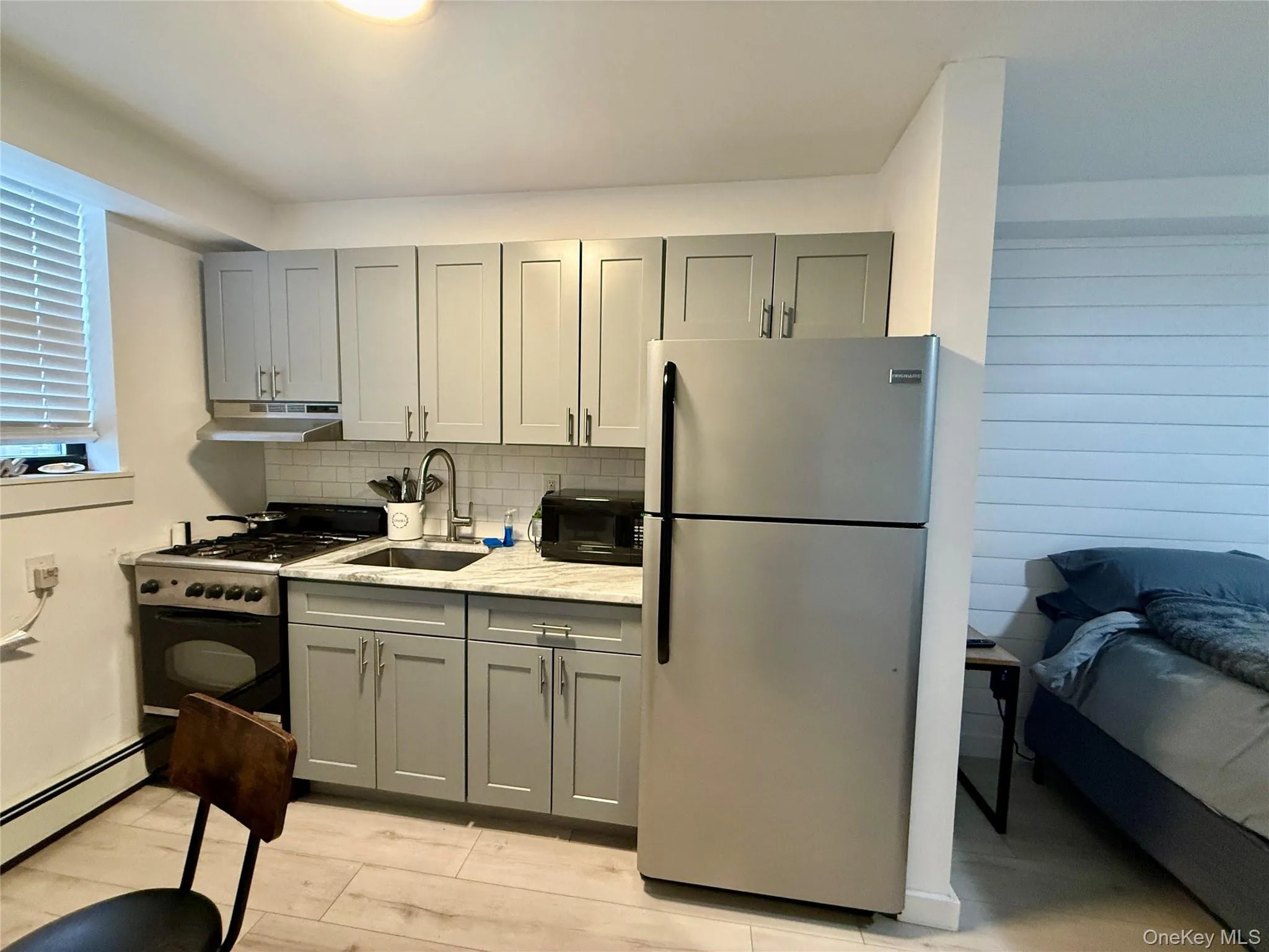 Kitchen with gray cabinets, freestanding refrigerator, range with gas stovetop, light stone counters, and under cabinet range hood Kitchen with gray cabinets, freestanding refrigerator, range with gas stovetop, light stone counters, and under cabinet range hood