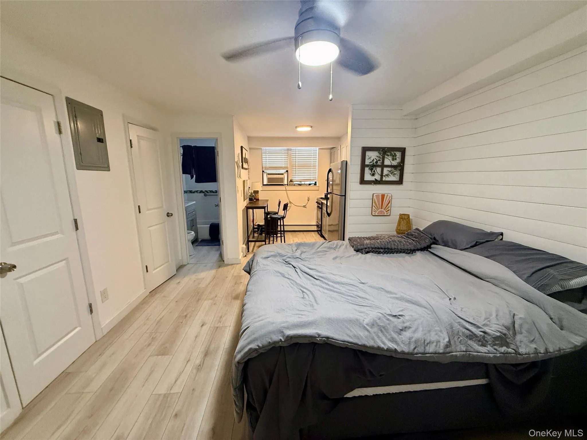 Bedroom with electric panel, light wood-style flooring, freestanding refrigerator, a ceiling fan, and ensuite bathroom Bedroom with electric panel, light wood-style flooring, freestanding refrigerator, a ceiling fan, and ensuite bathroom