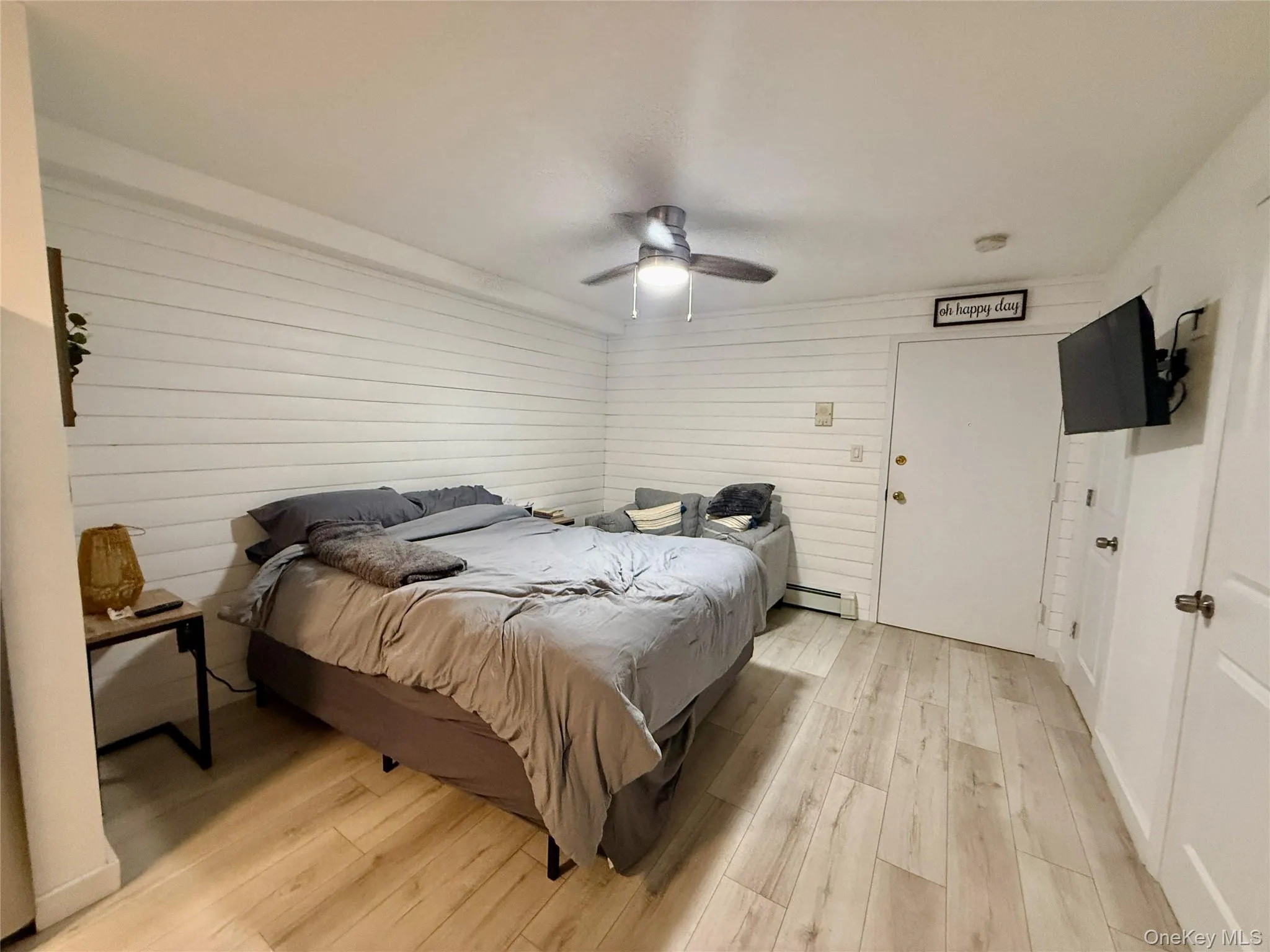Bedroom with light wood finished floors, ceiling fan, and a baseboard heating unit Bedroom with light wood finished floors, ceiling fan, and a baseboard heating unit