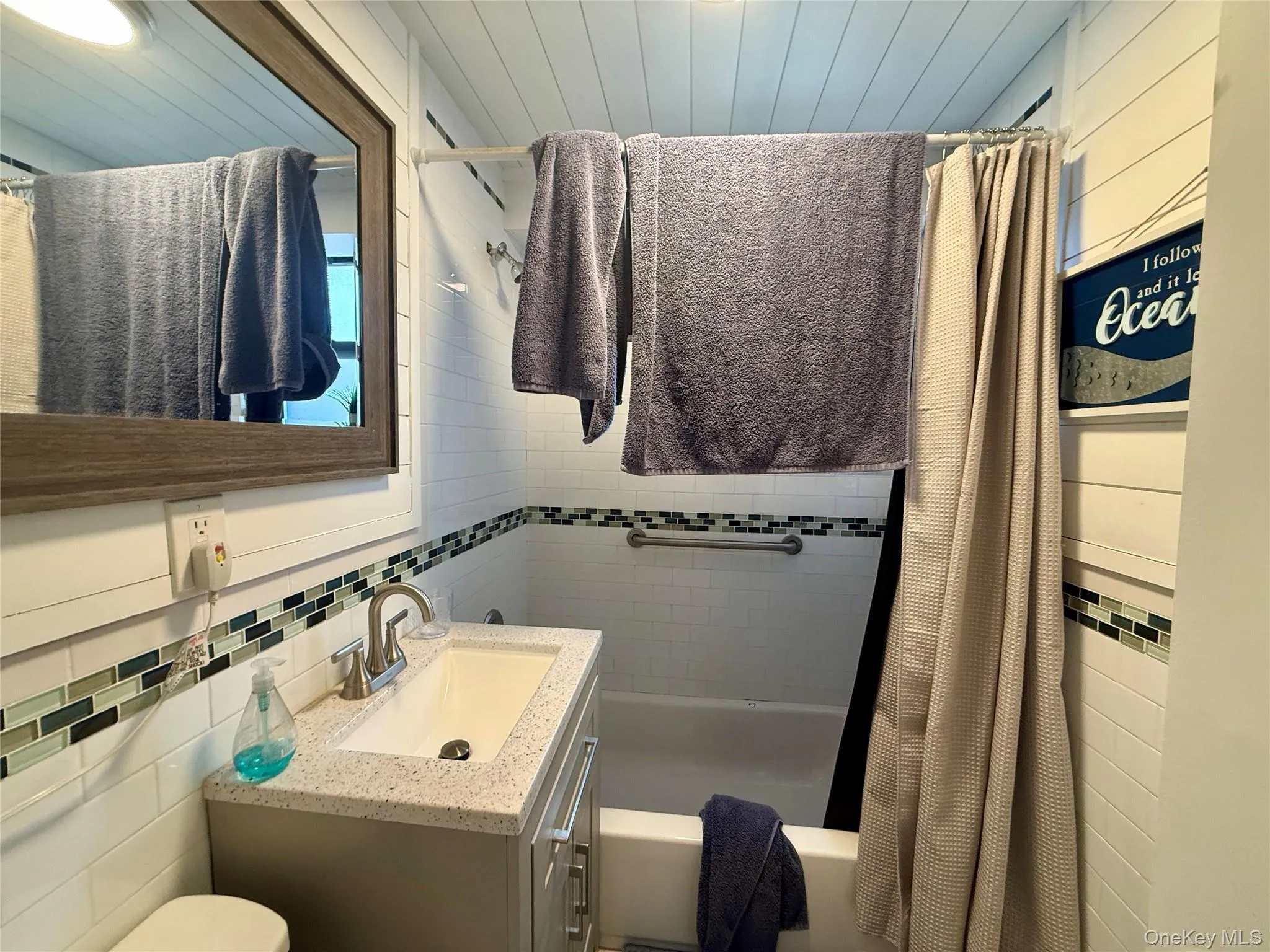 Bathroom featuring tile walls, vanity, shower / tub combo with curtain, and decorative backsplash Bathroom featuring tile walls, vanity, shower / tub combo with curtain, and decorative backsplash