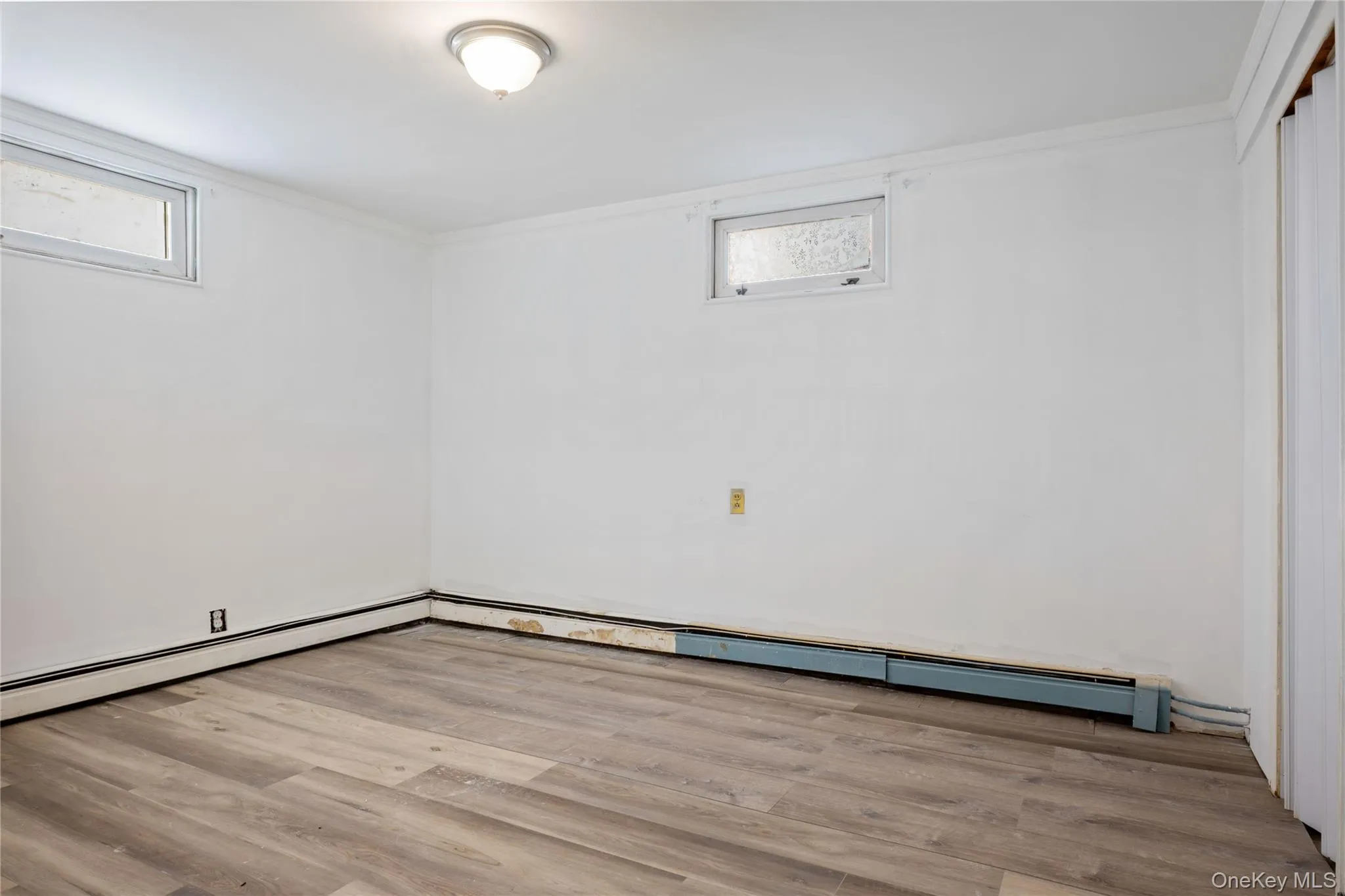 Basement with wood finished floors, a baseboard radiator, and crown molding Basement with wood finished floors, a baseboard radiator, and crown molding