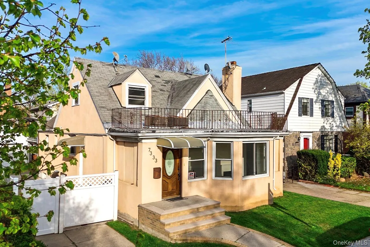 View of front facade with a front lawn, a chimney, concrete driveway, a garage, and a balcony View of front facade with a front lawn, a chimney, concrete driveway, a garage, and a balcony