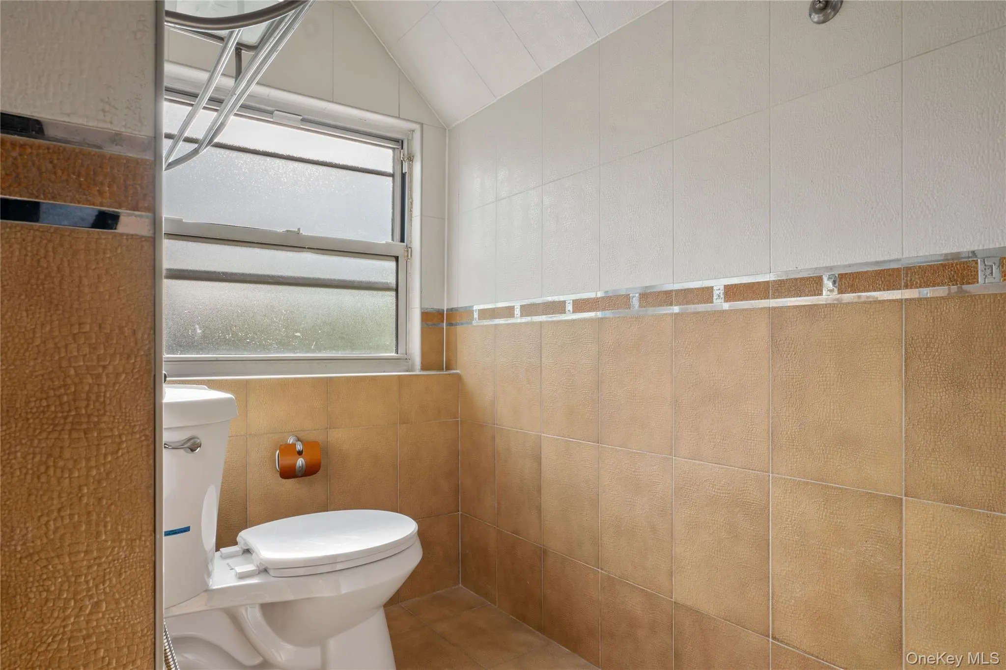 Bathroom with tile walls, lofted ceiling, and toilet Bathroom with tile walls, lofted ceiling, and toilet