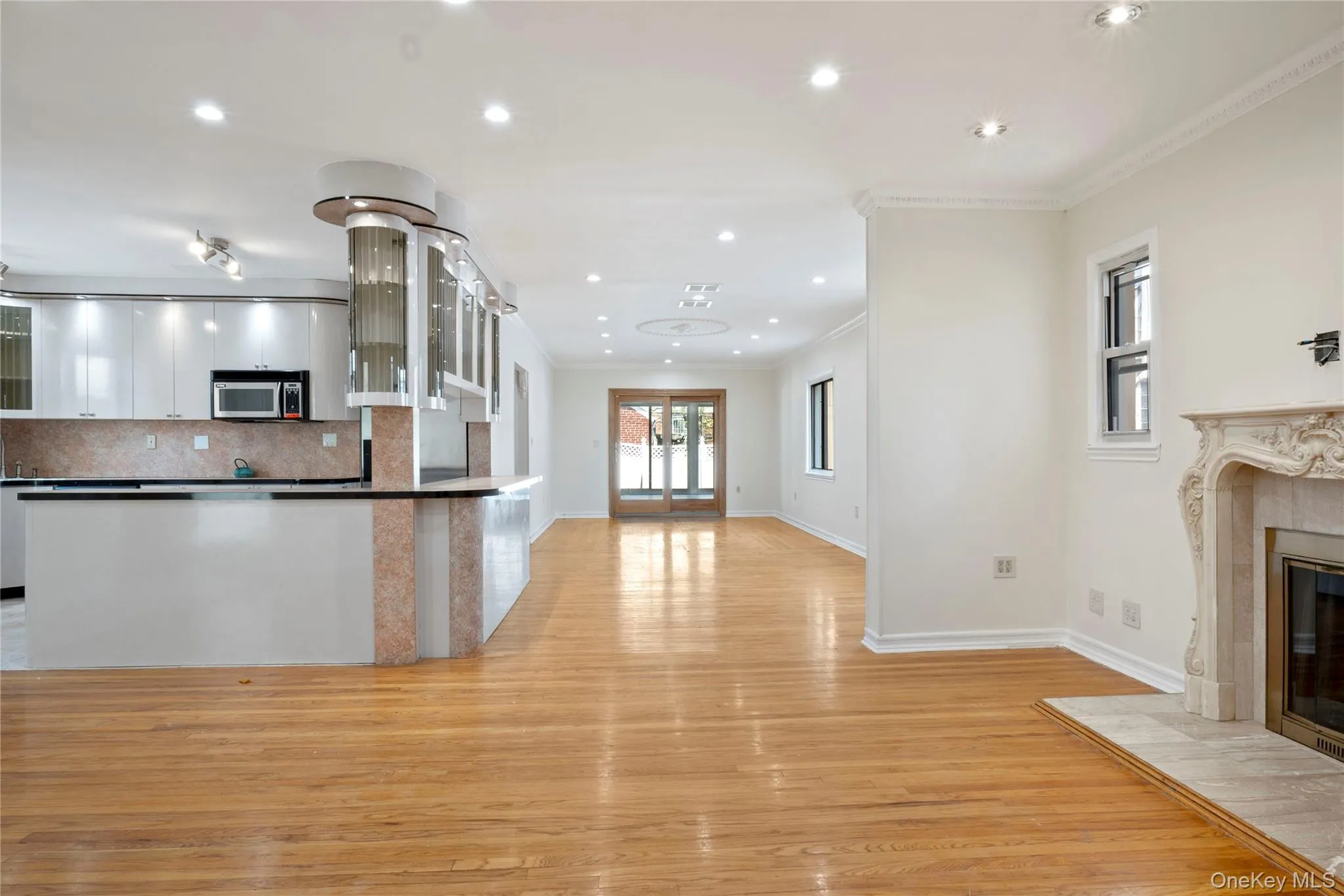 Kitchen featuring crown molding, a fireplace, white cabinets, stainless steel microwave, and light wood-style floors Kitchen featuring crown molding, a fireplace, white cabinets, stainless steel microwave, and light wood-style floors