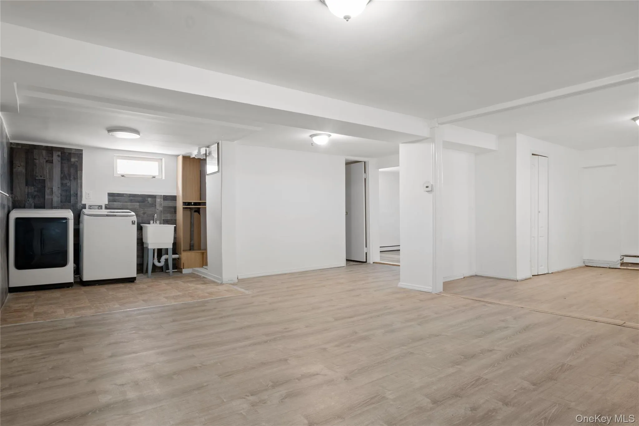 Below grade area featuring a baseboard heating unit, washing machine and clothes dryer, wood finished floors, and a sink Below grade area featuring a baseboard heating unit, washing machine and clothes dryer, wood finished floors, and a sink
