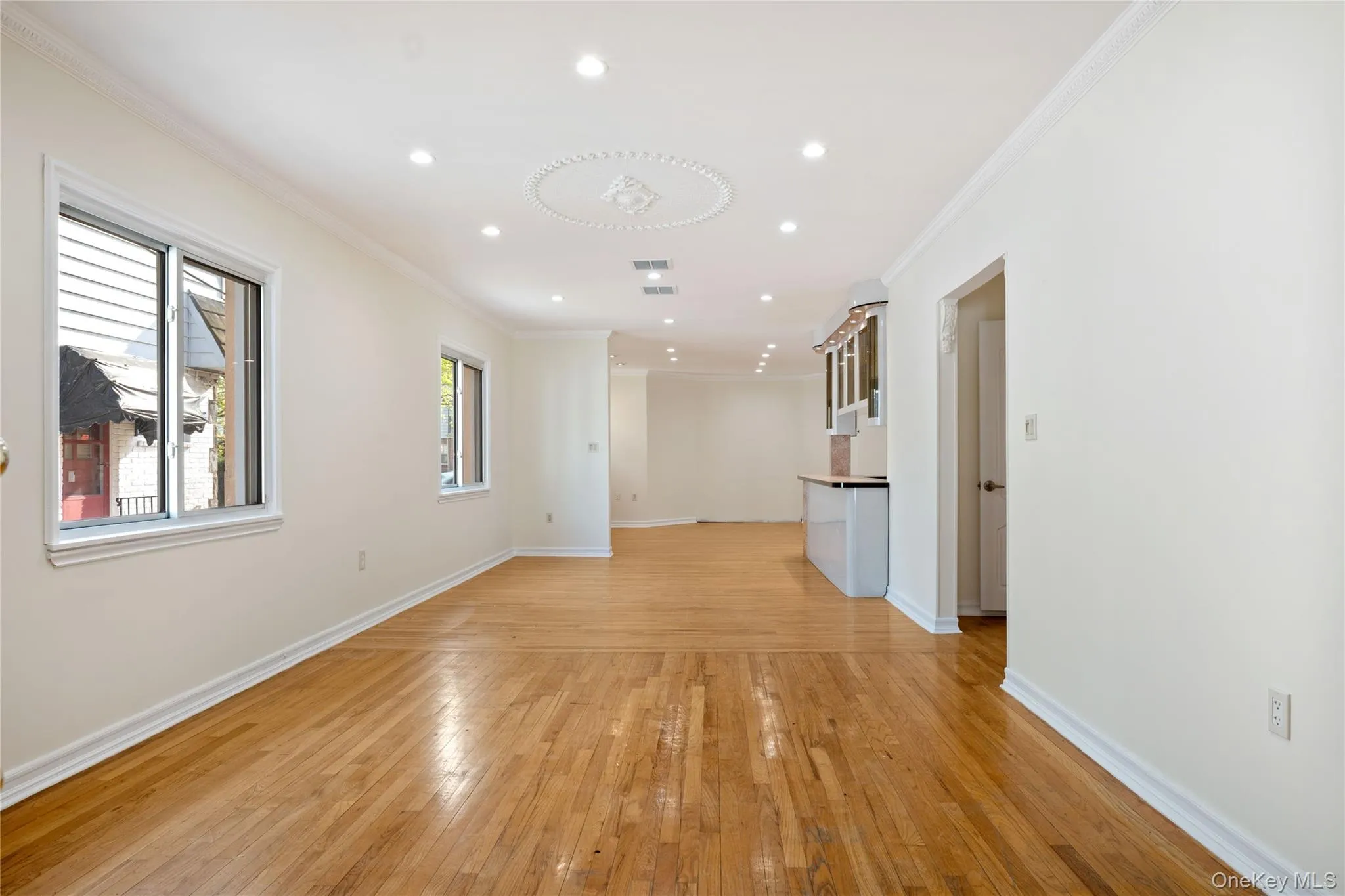 Unfurnished living room featuring recessed lighting, visible vents, ornamental molding, light wood-type flooring, and baseboards Unfurnished living room featuring recessed lighting, visible vents, ornamental molding, light wood-type flooring, and baseboards