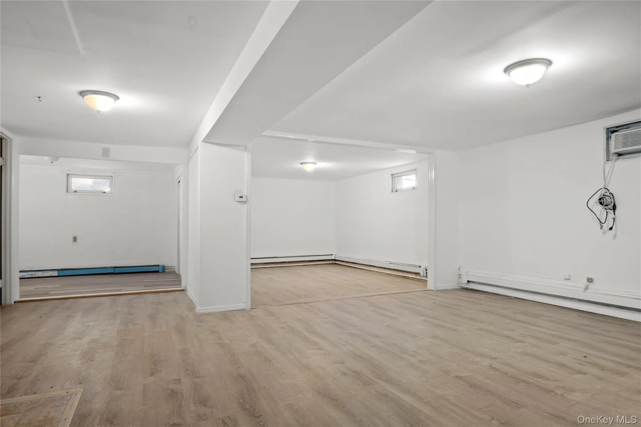 Below grade area featuring a baseboard heating unit, baseboards, wood finished floors, and a wall mounted air conditioner Below grade area featuring a baseboard heating unit, baseboards, wood finished floors, and a wall mounted air conditioner