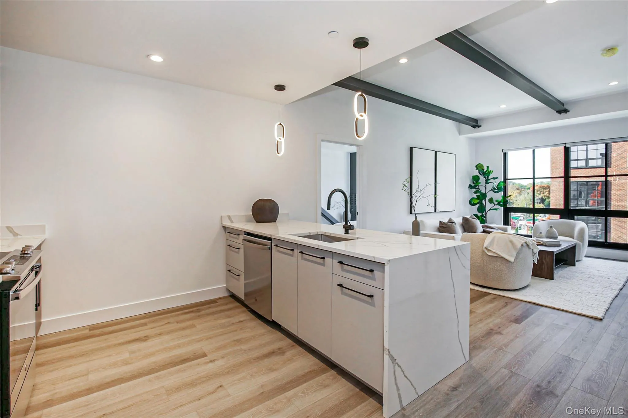Kitchen featuring stainless steel appliances, a peninsula, light wood-style flooring, beam ceiling, and light stone countertops Kitchen featuring stainless steel appliances, a peninsula, light wood-style flooring, beam ceiling, and light stone countertops