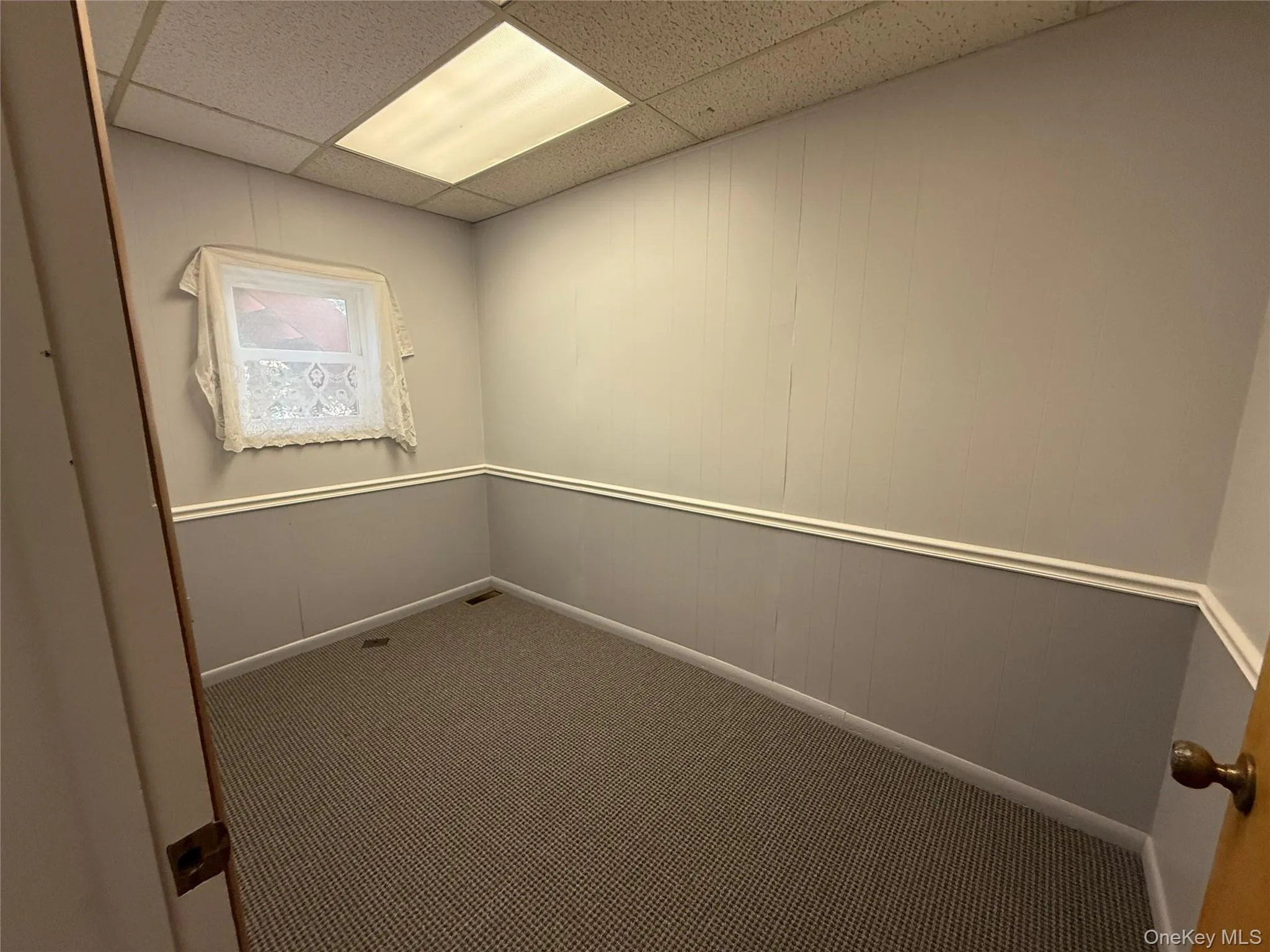 Unfurnished room with carpet floors, wood walls, and a paneled ceiling Unfurnished room with carpet floors, wood walls, and a paneled ceiling