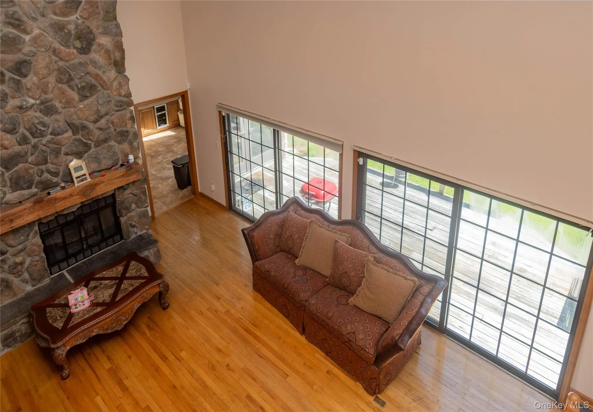 Living room with a high ceiling, light wood finished floors, and a stone fireplace Living room with a high ceiling, light wood finished floors, and a stone fireplace