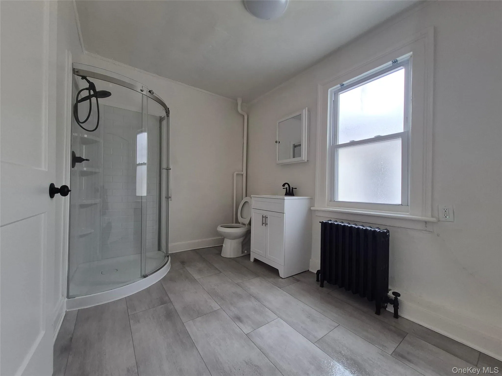 Bathroom featuring a shower stall, radiator, vanity, and wood finish floors Bathroom featuring a shower stall, radiator, vanity, and wood finish floors