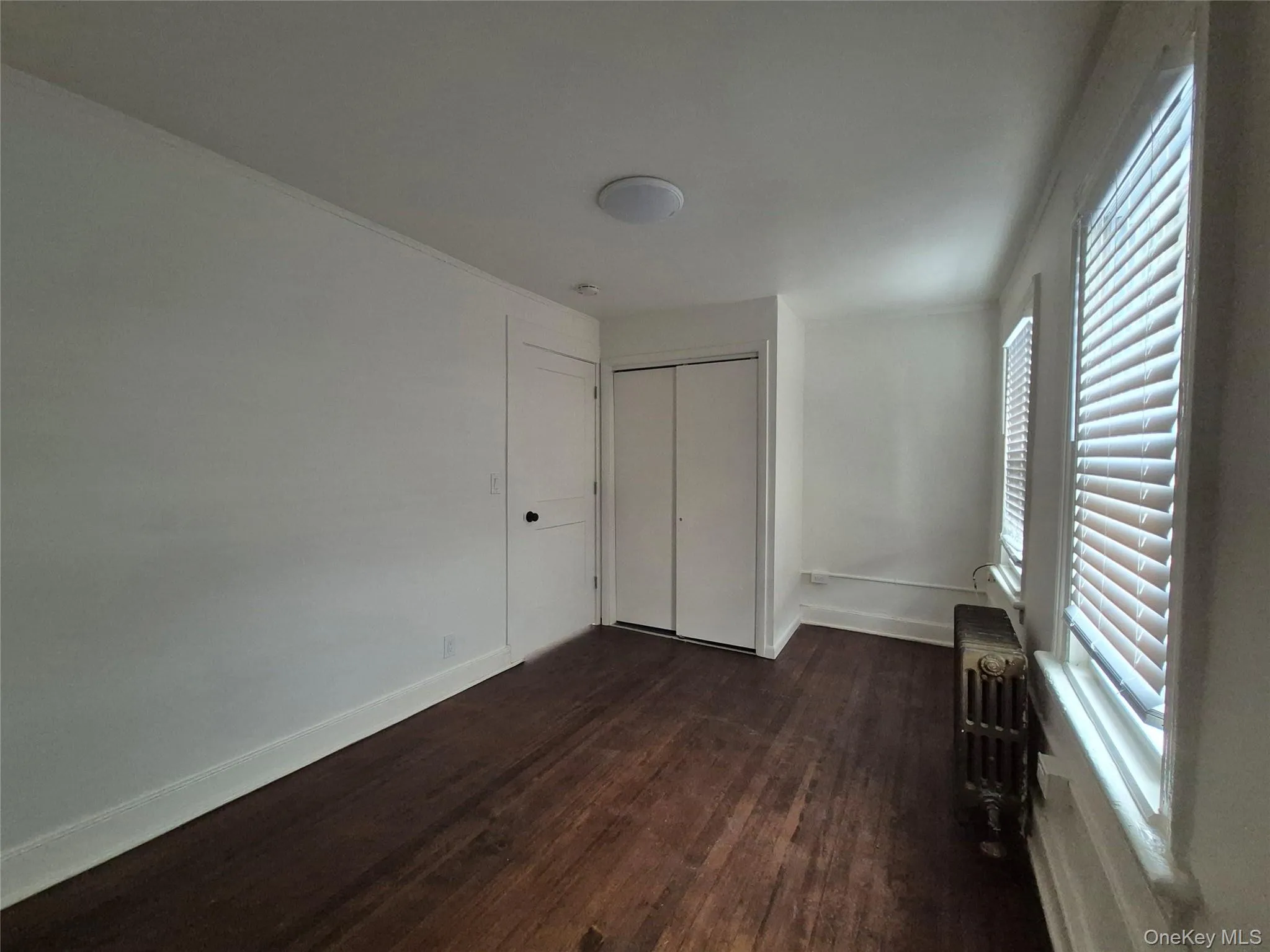 Unfurnished bedroom with dark wood finished floors, radiator, and a closet Unfurnished bedroom with dark wood finished floors, radiator, and a closet