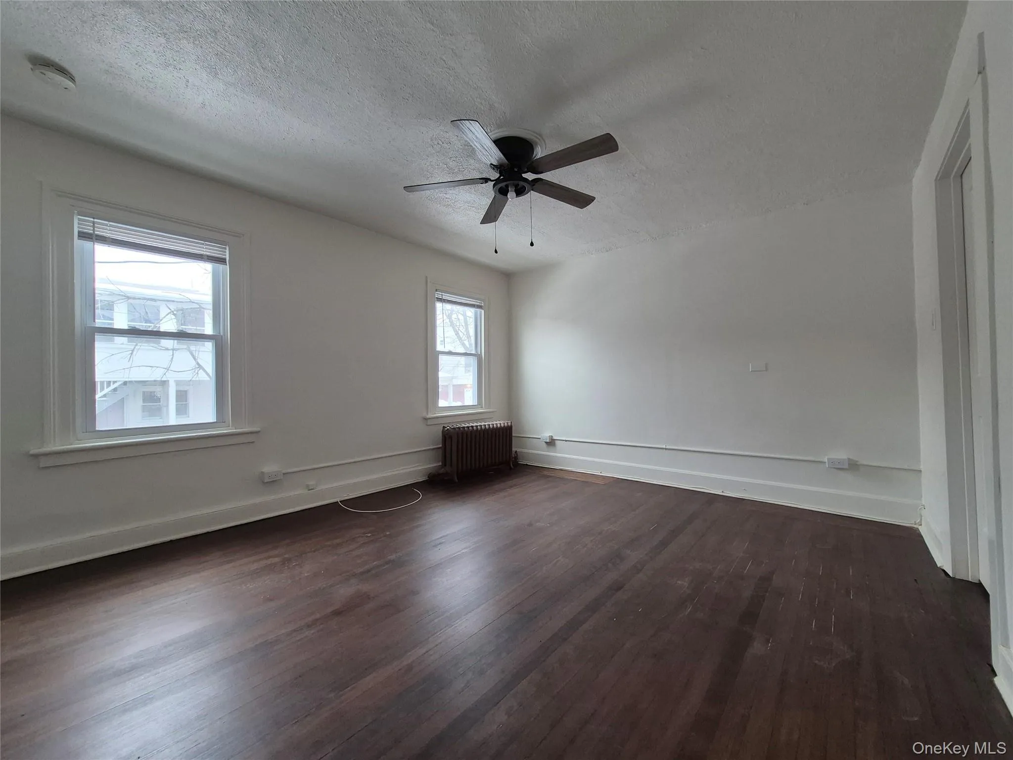 Unfurnished room with radiator, dark wood-type flooring, ceiling fan, and a textured ceiling Unfurnished room with radiator, dark wood-type flooring, ceiling fan, and a textured ceiling