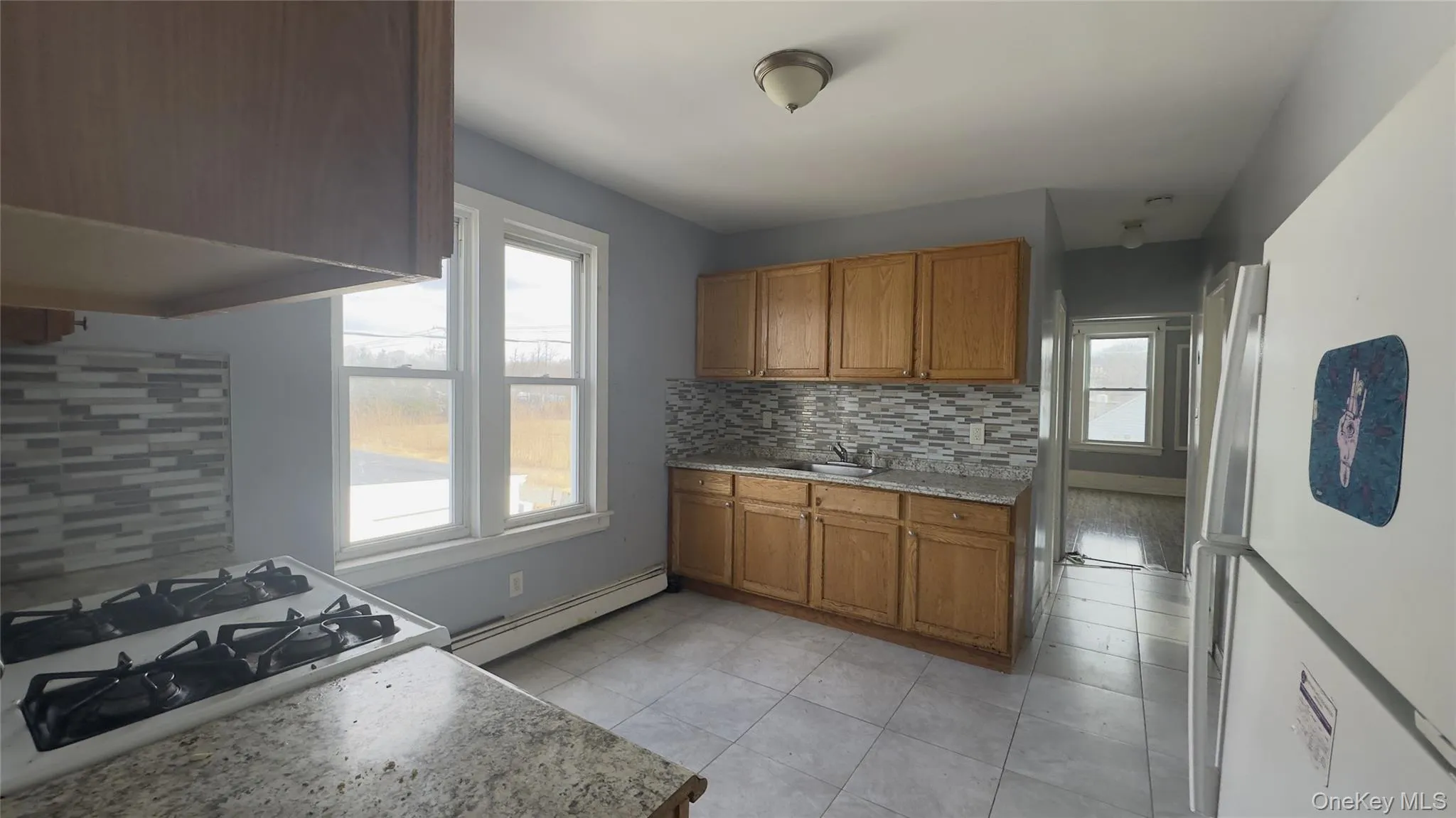 Kitchen featuring brown cabinets, white appliances, backsplash, baseboard heating, and light tile patterned floors Kitchen featuring brown cabinets, white appliances, backsplash, baseboard heating, and light tile patterned floors