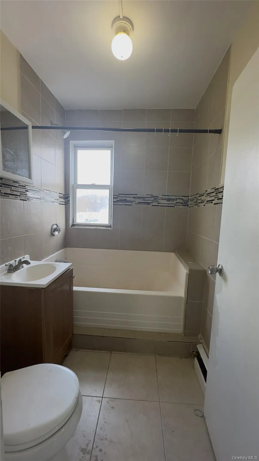 Bathroom featuring bathtub / shower combination, vanity, tile walls, light tile patterned floors, and a baseboard radiator Bathroom featuring bathtub / shower combination, vanity, tile walls, light tile patterned floors, and a baseboard radiator