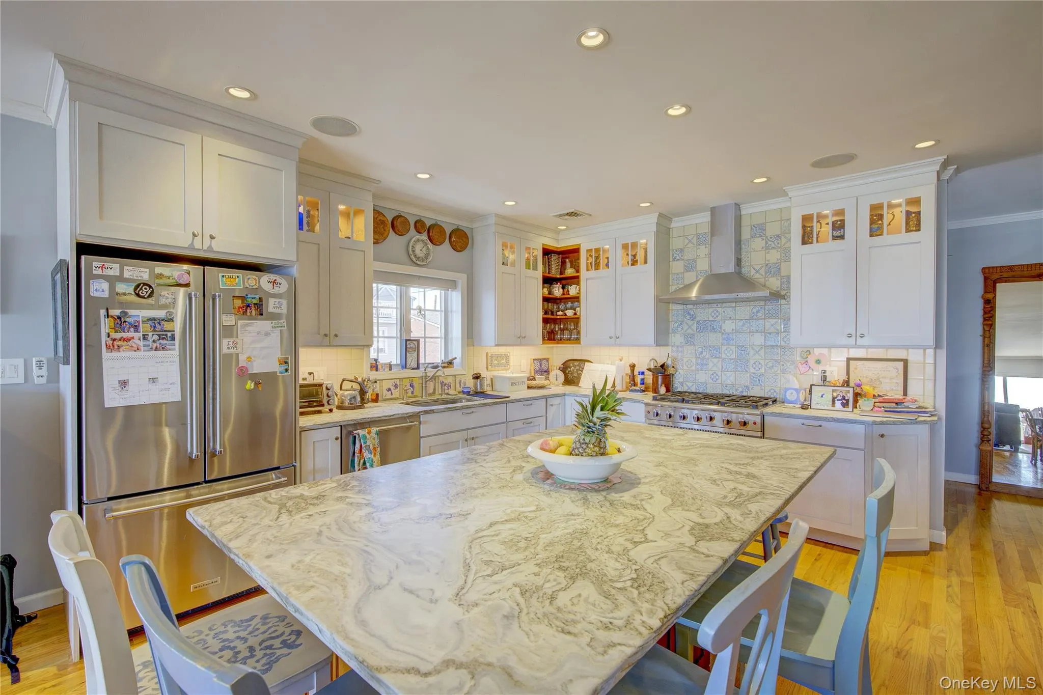 Kitchen featuring wall chimney range hood, a kitchen bar, stainless steel appliances, and light wood-style flooring Kitchen featuring wall chimney range hood, a kitchen bar, stainless steel appliances, and light wood-style flooring