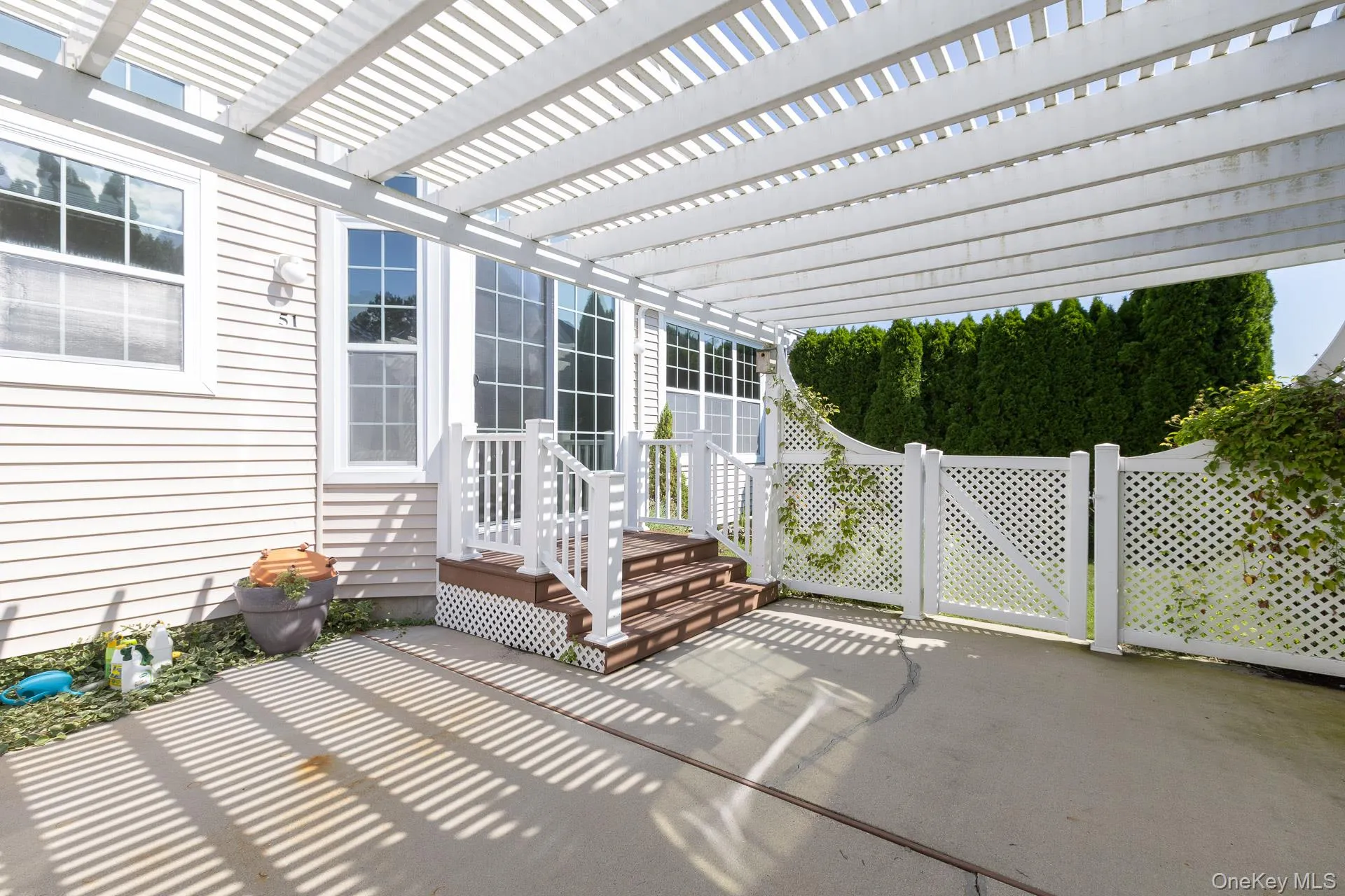 Expansive concrete patio with a white pergola and lattice fencing Expansive concrete patio with a white pergola and lattice fencing