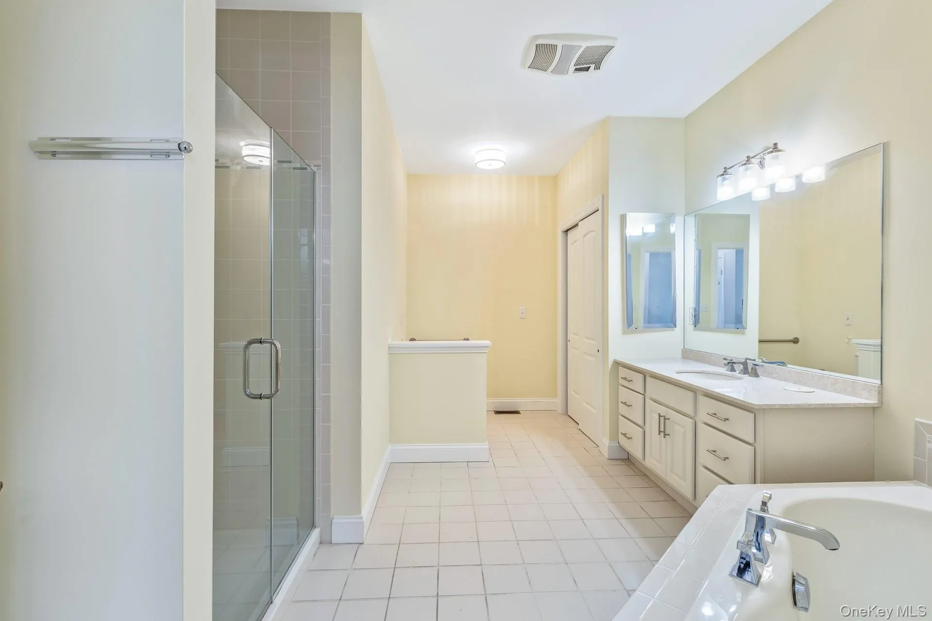 Walk-in shower with clear glass enclosure and tiled walls, dual vanity with undermount sinks and large mirror, built-in bathtub with deck-mounted faucet, and tiled flooring Walk-in shower with clear glass enclosure and tiled walls, dual vanity with undermount sinks and large mirror, built-in bathtub with deck-mounted faucet, and tiled flooring