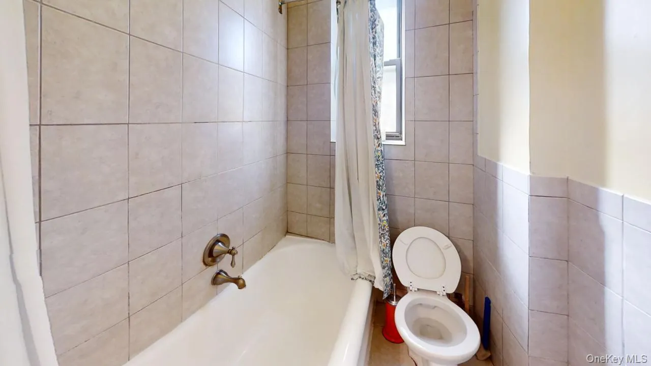 Bathroom with toilet, tile walls, and shower / tub combo with curtain Bathroom with toilet, tile walls, and shower / tub combo with curtain