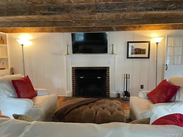 Living room area featuring beamed ceiling, a fireplace, wooden walls, and wood finished floors Living room area featuring beamed ceiling, a fireplace, wooden walls, and wood finished floors