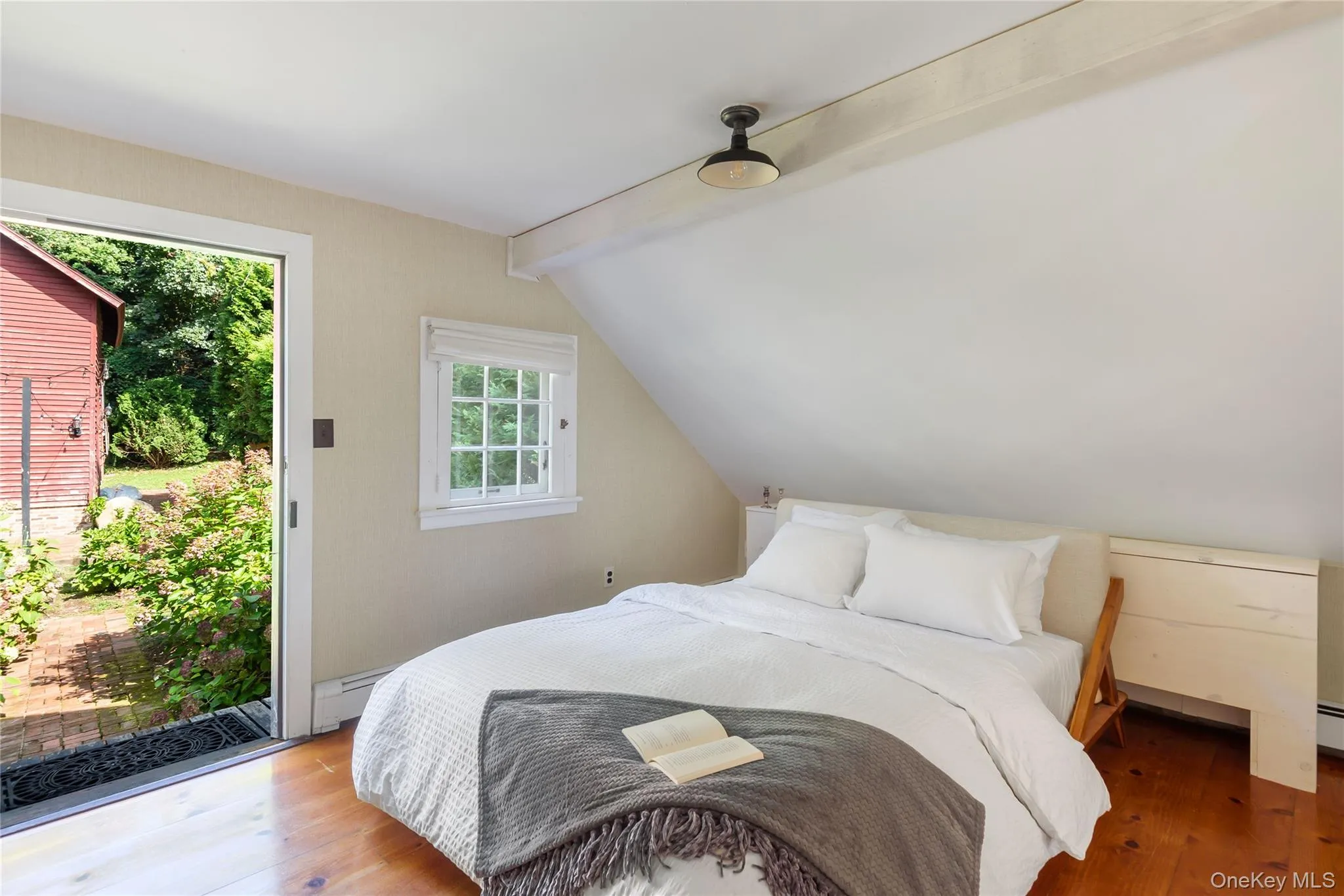 PRIMARY Bedroom with access to exterior, lofted ceiling with beams, wood finished floors, and a baseboard heating unit PRIMARY Bedroom with access to exterior, lofted ceiling with beams, wood finished floors, and a baseboard heating unit