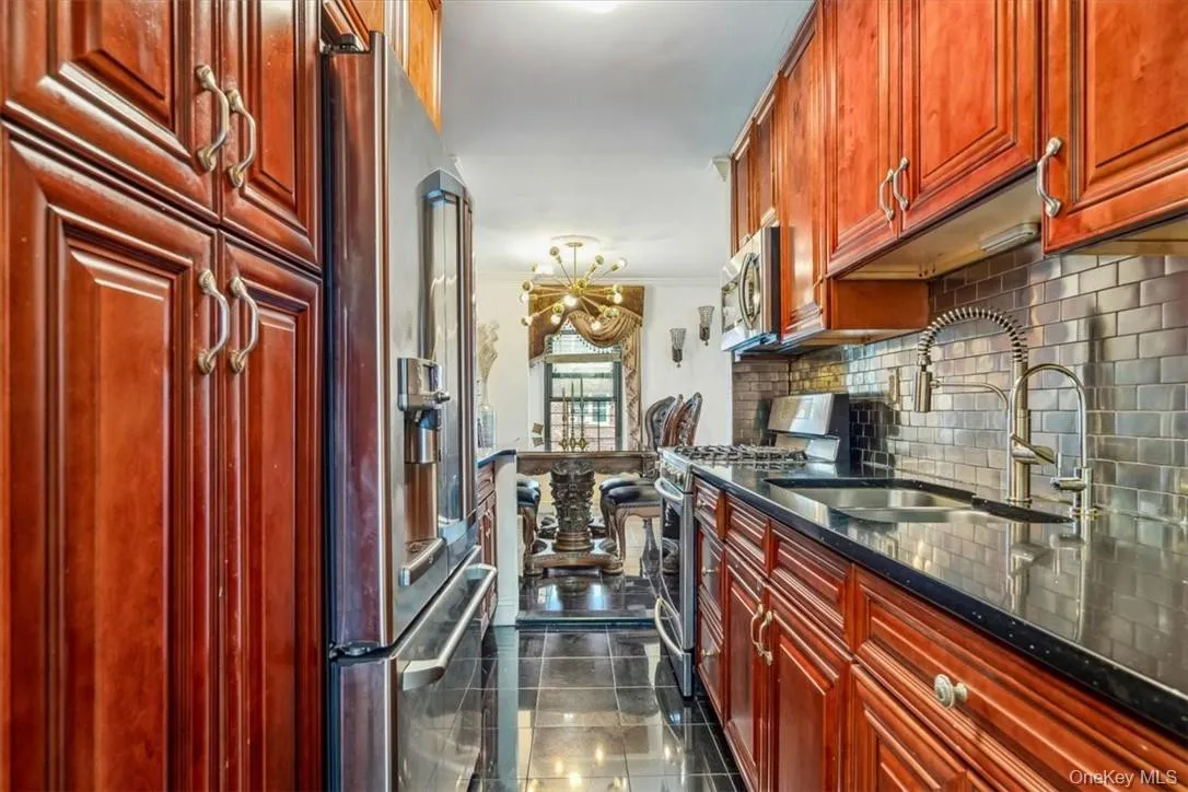 Kitchen with dark stone countertops, stainless steel appliances, sink, tasteful backsplash, and dark tile flooring Kitchen with dark stone countertops, stainless steel appliances, sink, tasteful backsplash, and dark tile flooring
