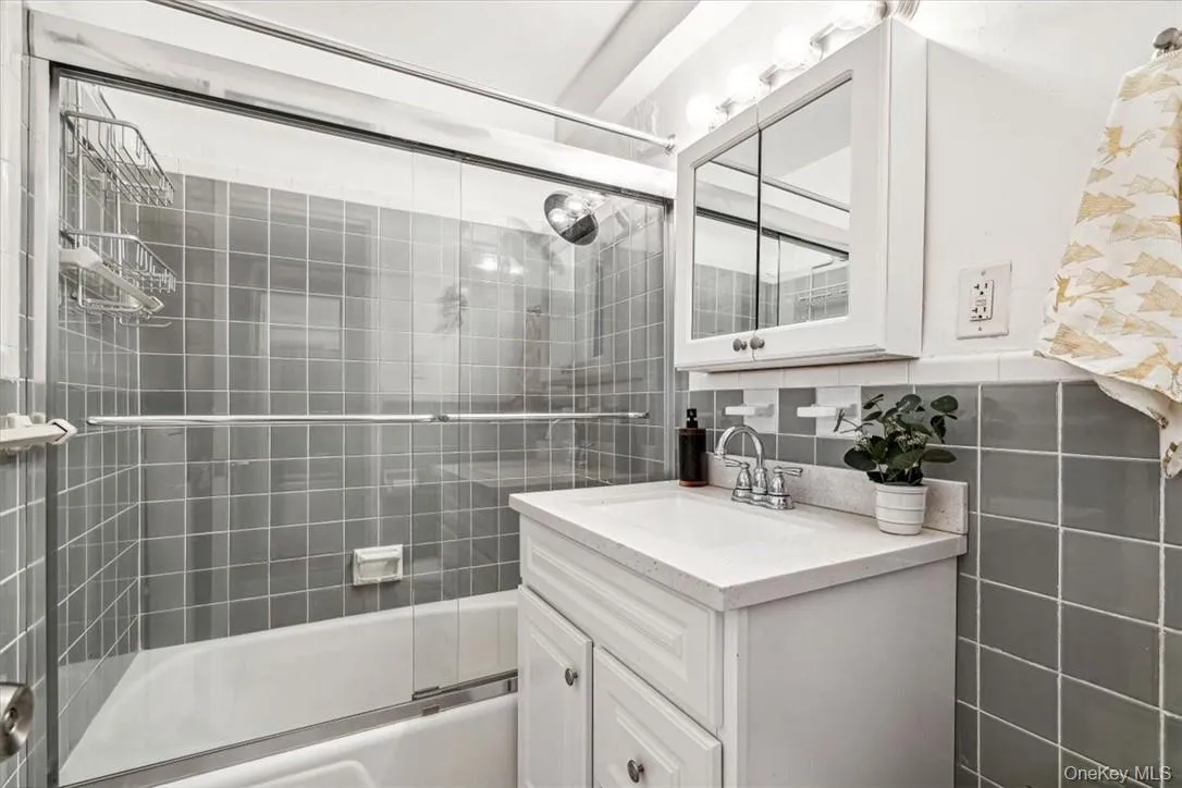 Bathroom with backsplash, vanity with extensive cabinet space, enclosed tub / shower combo, and tile walls Bathroom with backsplash, vanity with extensive cabinet space, enclosed tub / shower combo, and tile walls