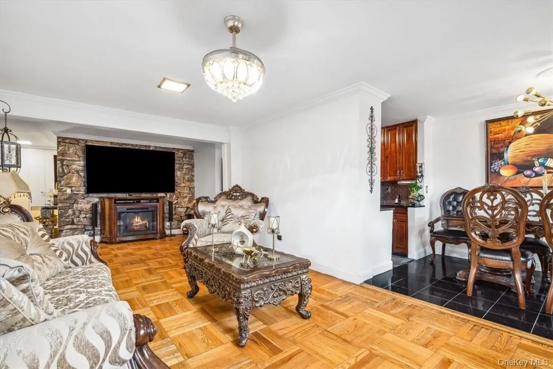 Living room featuring a stone fireplace, ornamental molding, parquet floors, and an inviting chandelier Living room featuring a stone fireplace, ornamental molding, parquet floors, and an inviting chandelier
