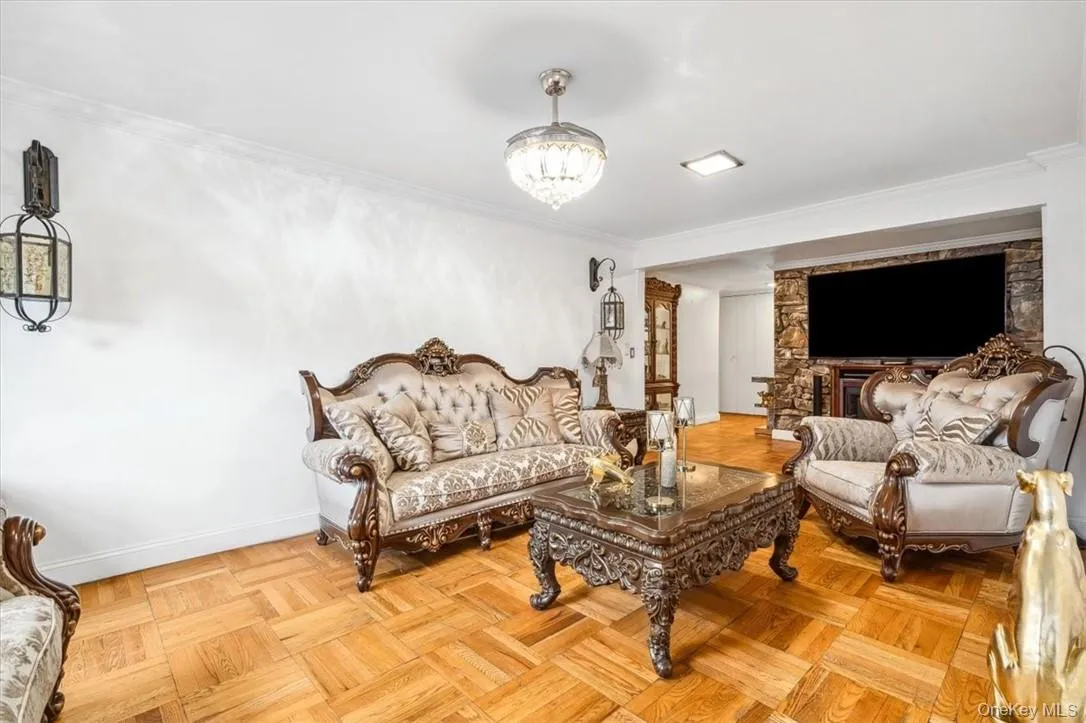 Living room with a stone fireplace, a chandelier, crown molding, and light parquet floors Living room with a stone fireplace, a chandelier, crown molding, and light parquet floors